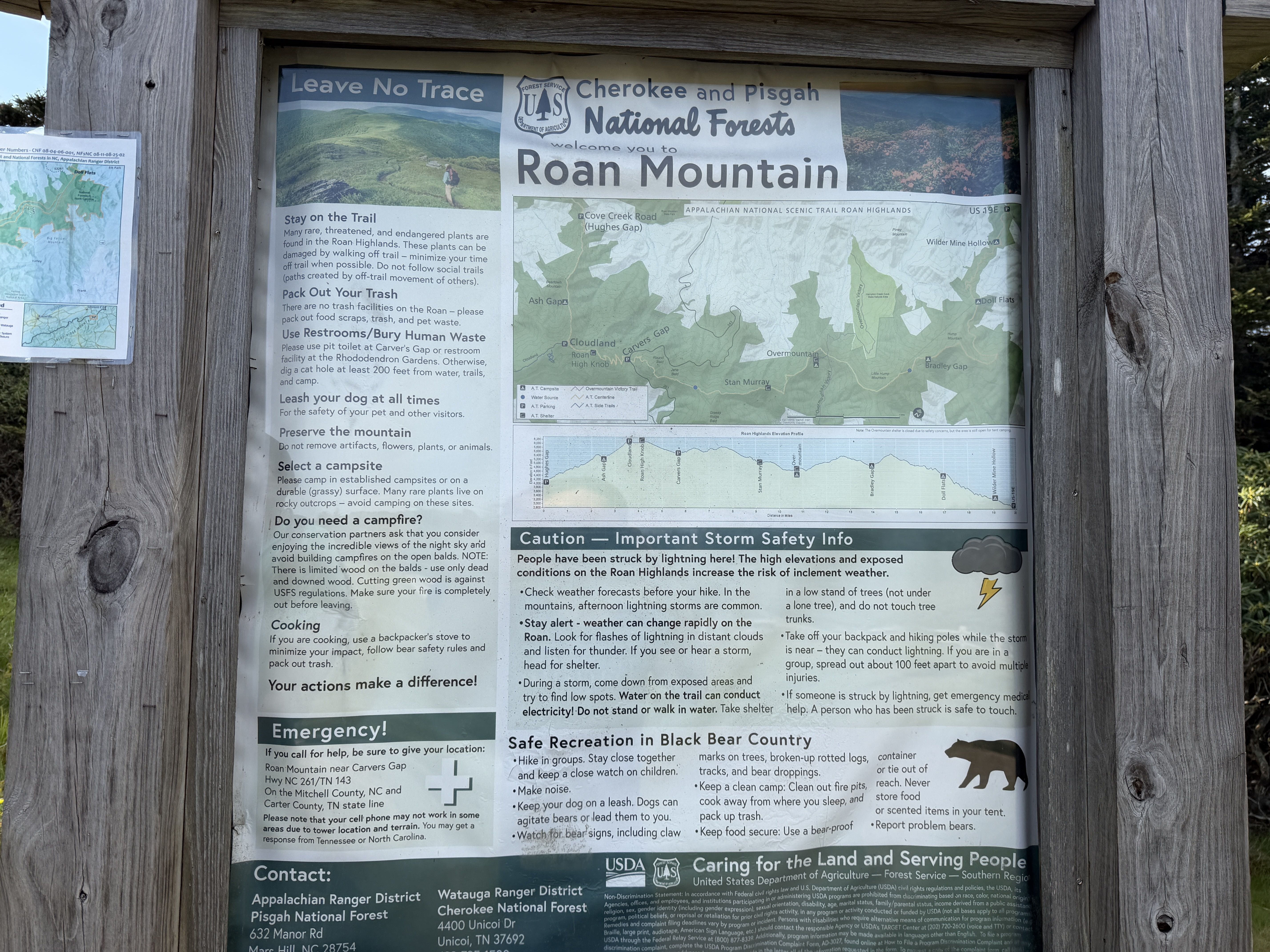 Wooden bulletin board displaying a Roan Mountain map and safety signs for Cherokee and Pisgah National Forests, with a "Leave No Trace" banner and a hiker image.