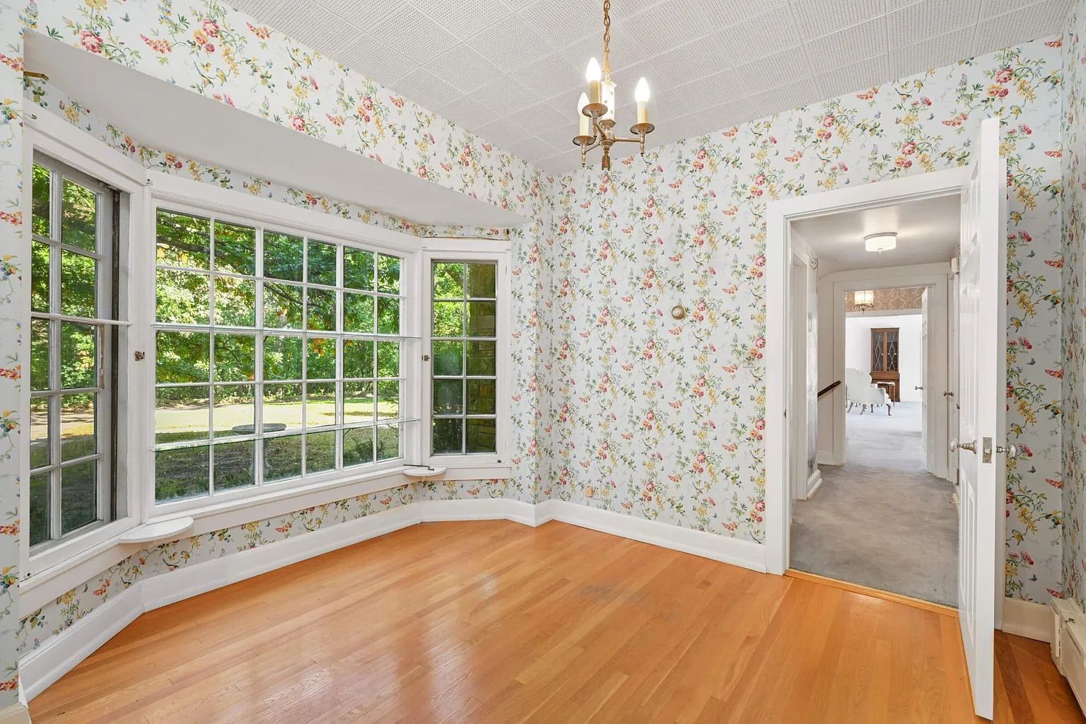 An empty room with a bay window and floral wallpaper.
