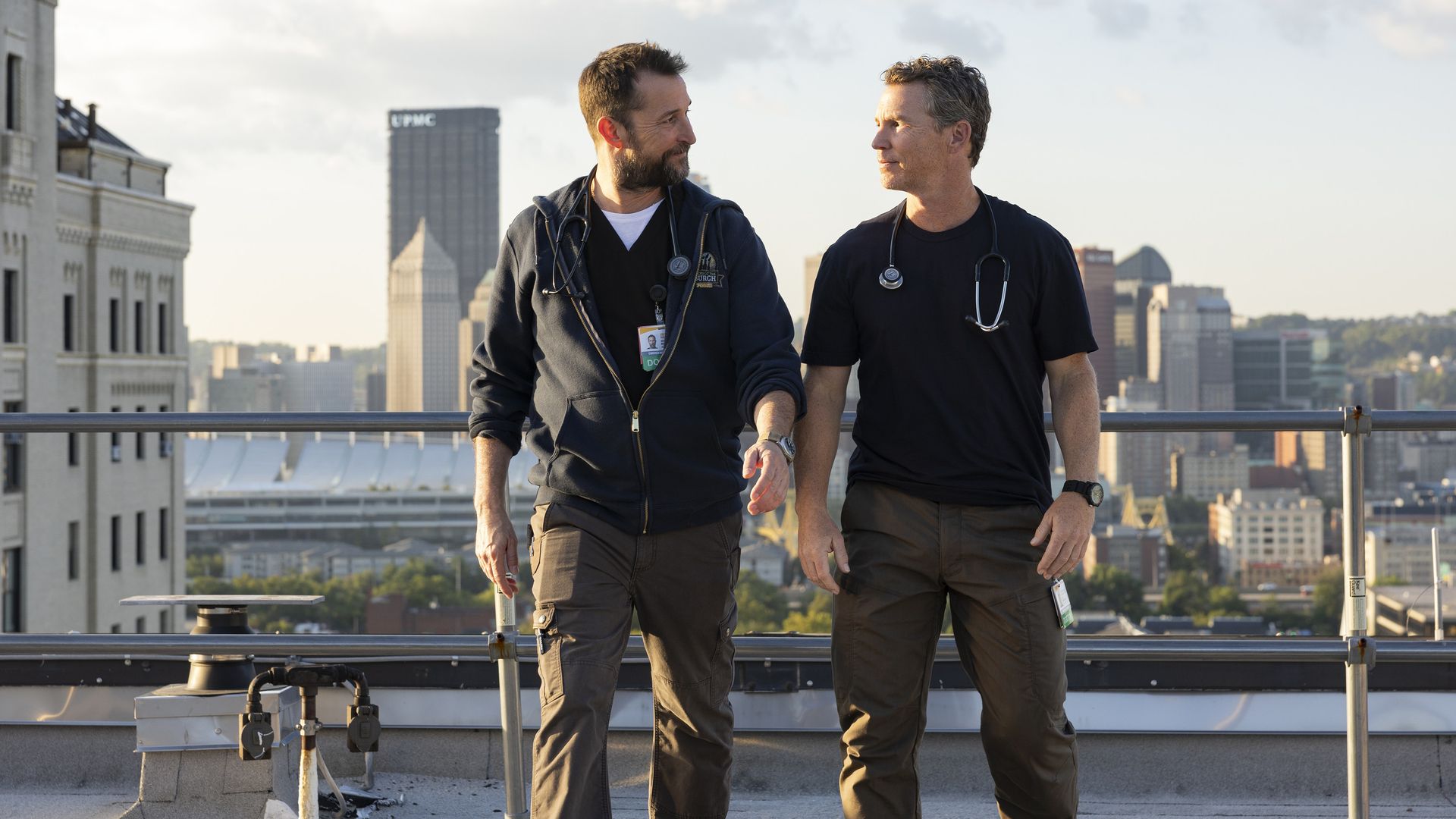 Noah Wyle and Shawn Hatosy on set of "The Pitt" with the Pittsburgh skyline in the background