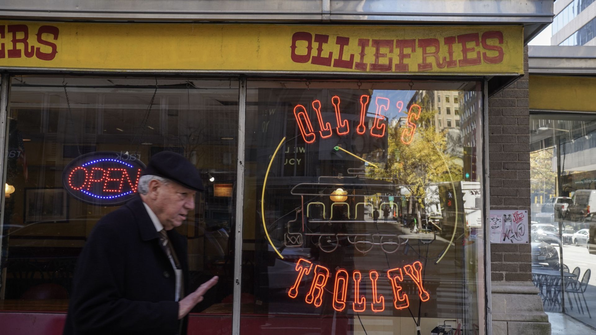 A man walks past a storefront that reads "Ollie's Trolley" in neon letters. 