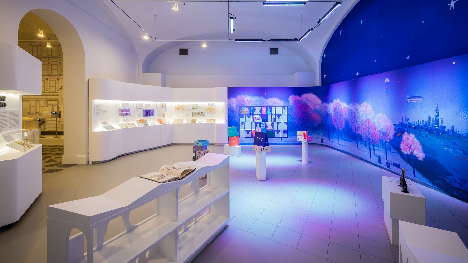 A room in a museum with exhibits along one wall and an interactive display against the other.