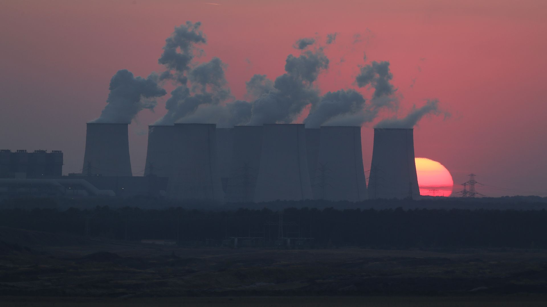 A power plant producing lots of smoke in front of a beautiful, red sunset