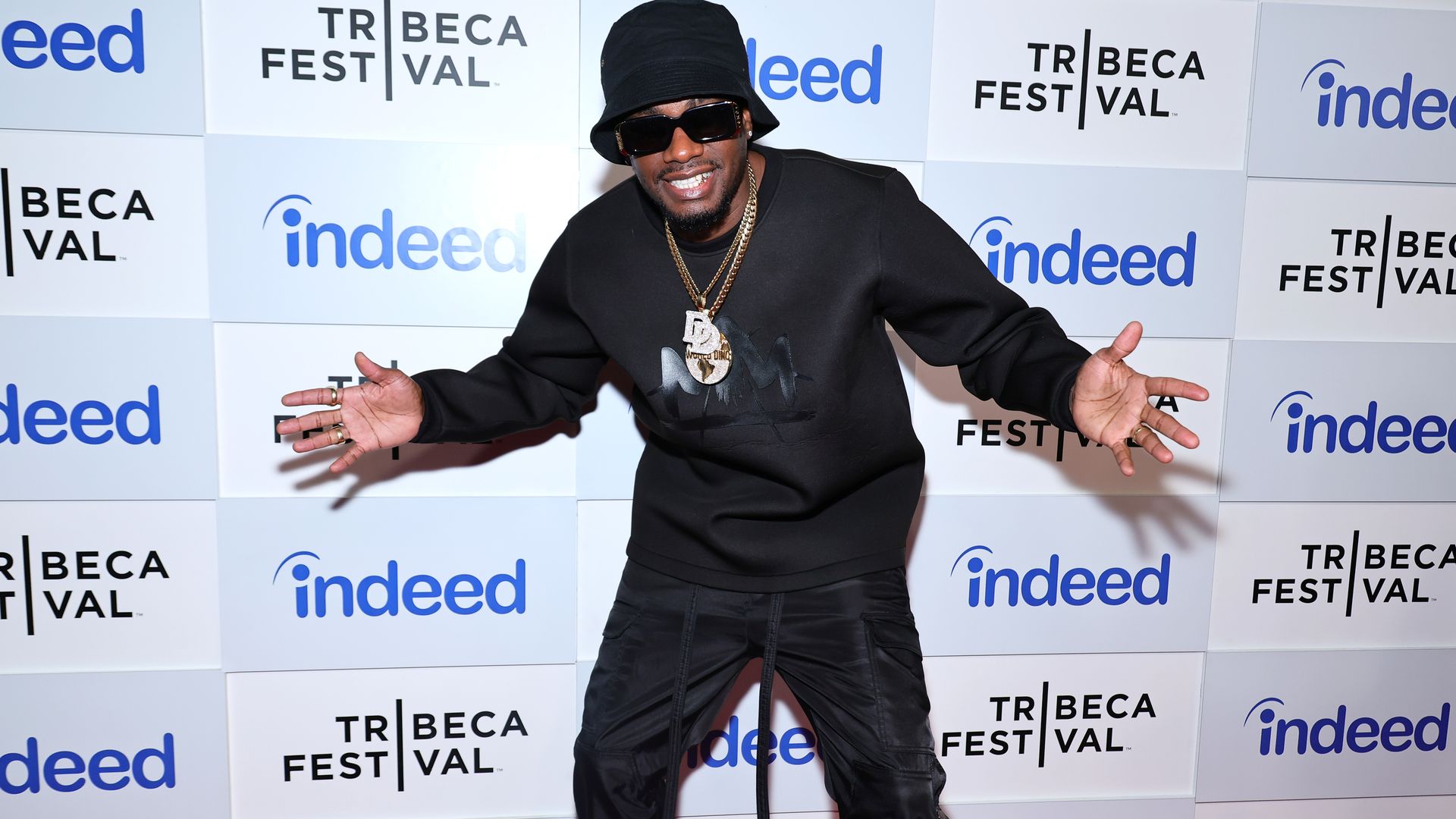 A man in a black outfit sticks his hands out in a fun pose
