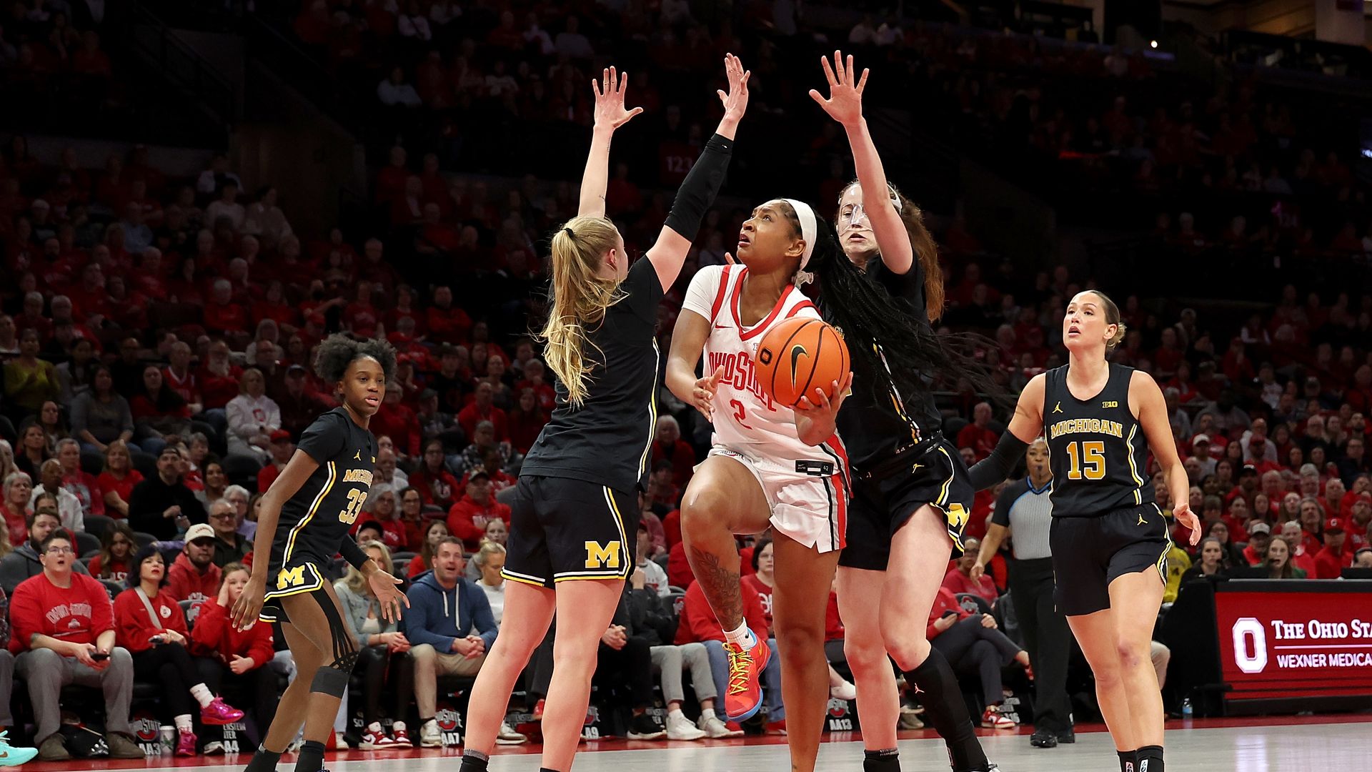 Chance Gray #2 of the Ohio State Buckeyes shoots the ball while being defended by Olivia Olson #1 of the Michigan Wolverines and Syla Swords #12