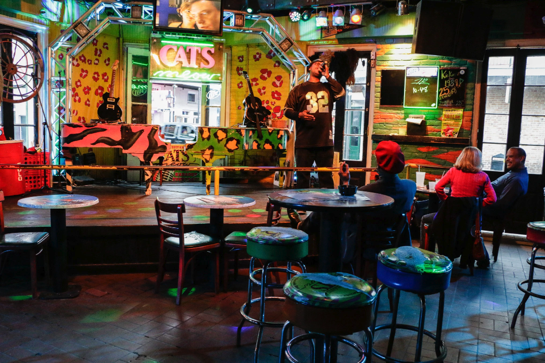 Photo shows someone singing karaoke on the colorful Cats Meow stage in New Orleans.