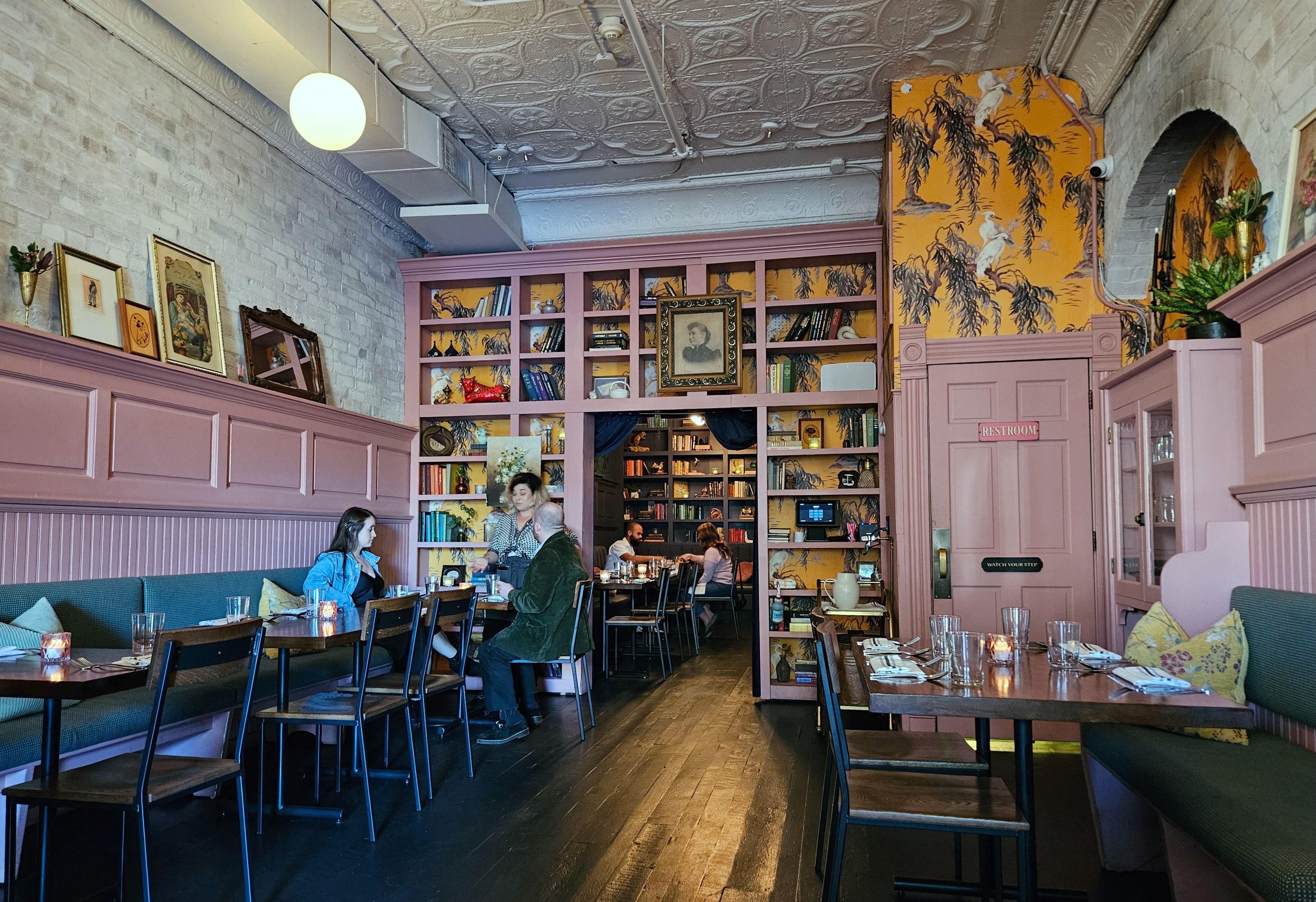 The interior of Chapman's Eat Market, with pink walls and bookshelves surrounding tables in the dining area, which has wood floors