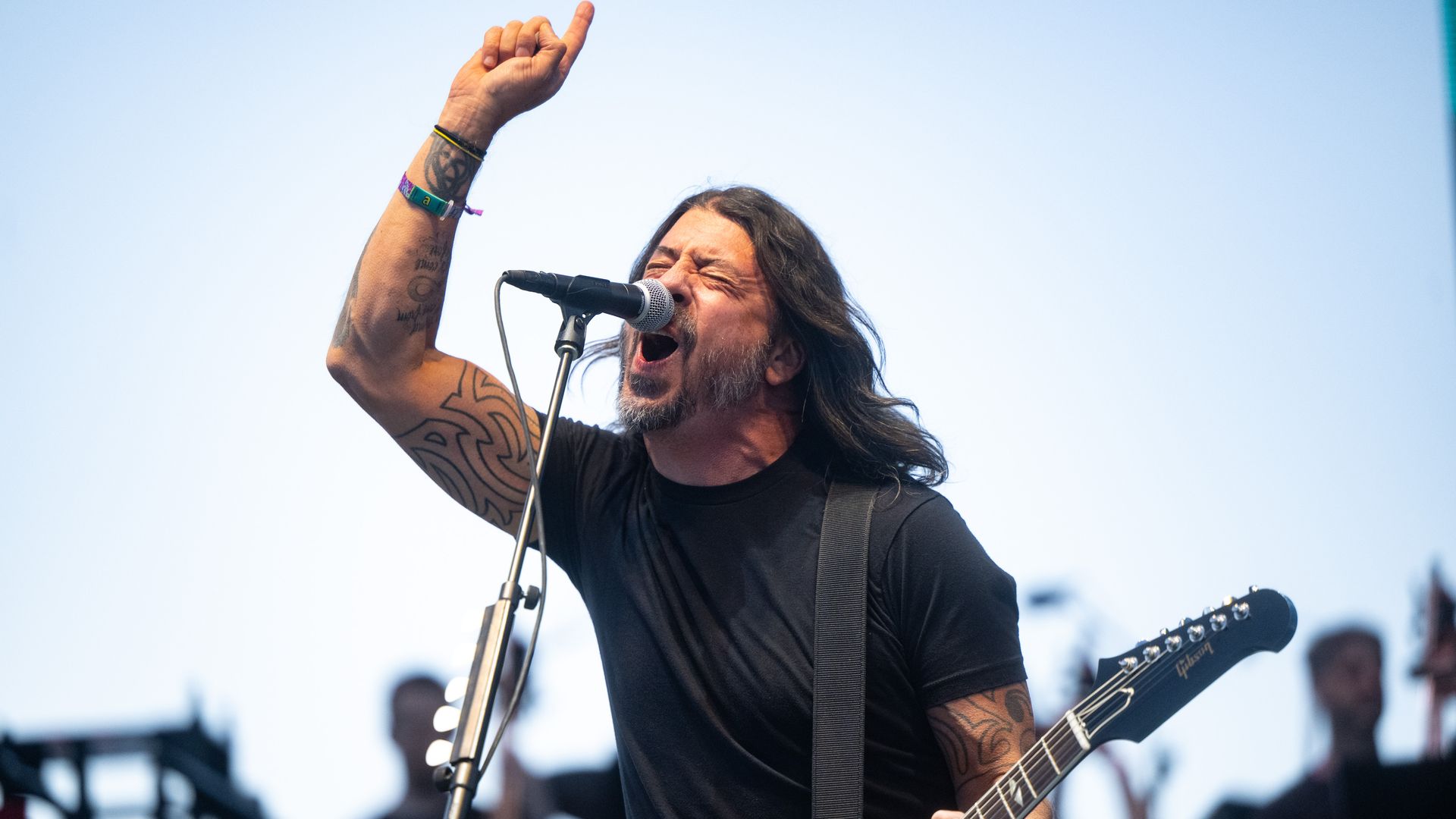 Musician Dave Grohl performs on stage with his finger in the air while singing into a microphone and playing guitar. 