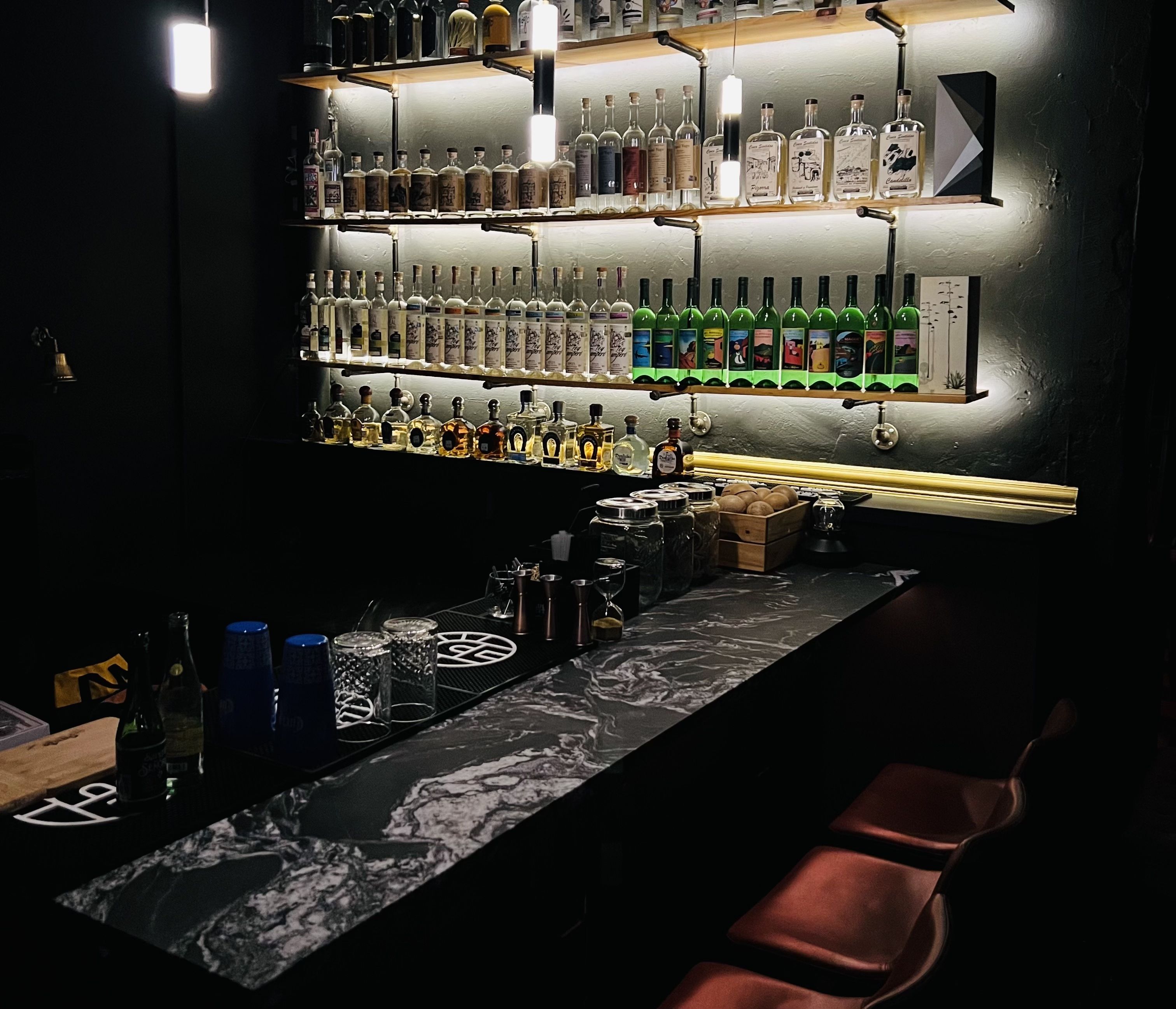 A low-lit bar with marble countertops and shelves lined with various bottles of alcohol. 
