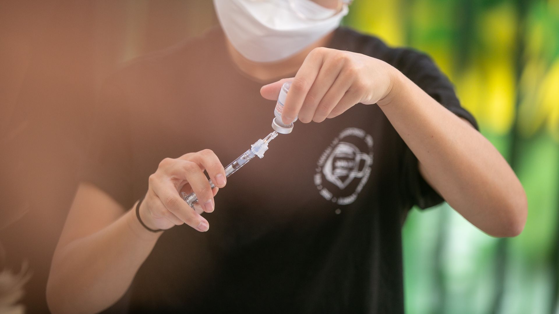Photo of a masked health care worker holding up a COVID vaccine needle