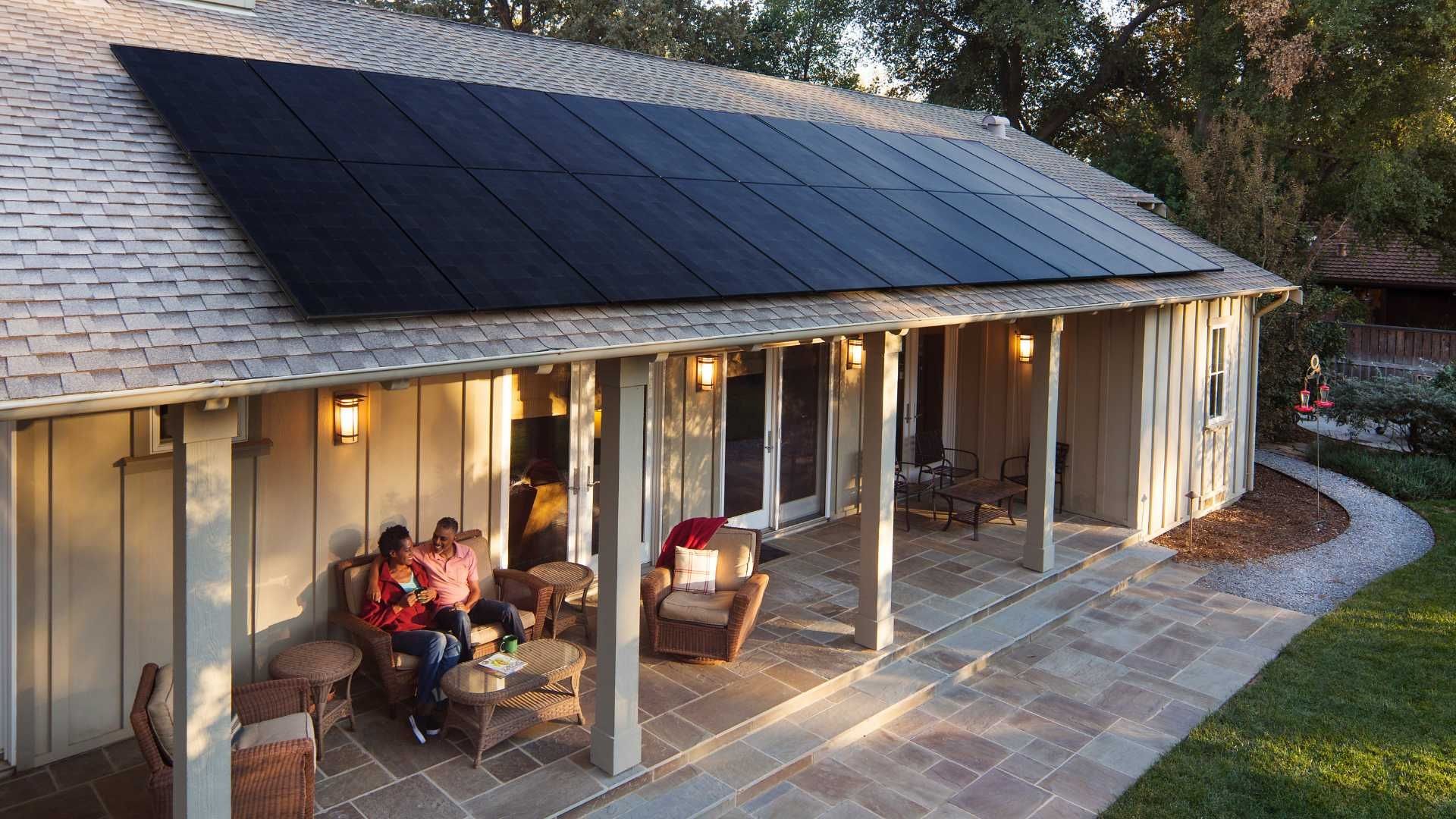 Two people sitting on a house porch. There are solar panels on the roof.