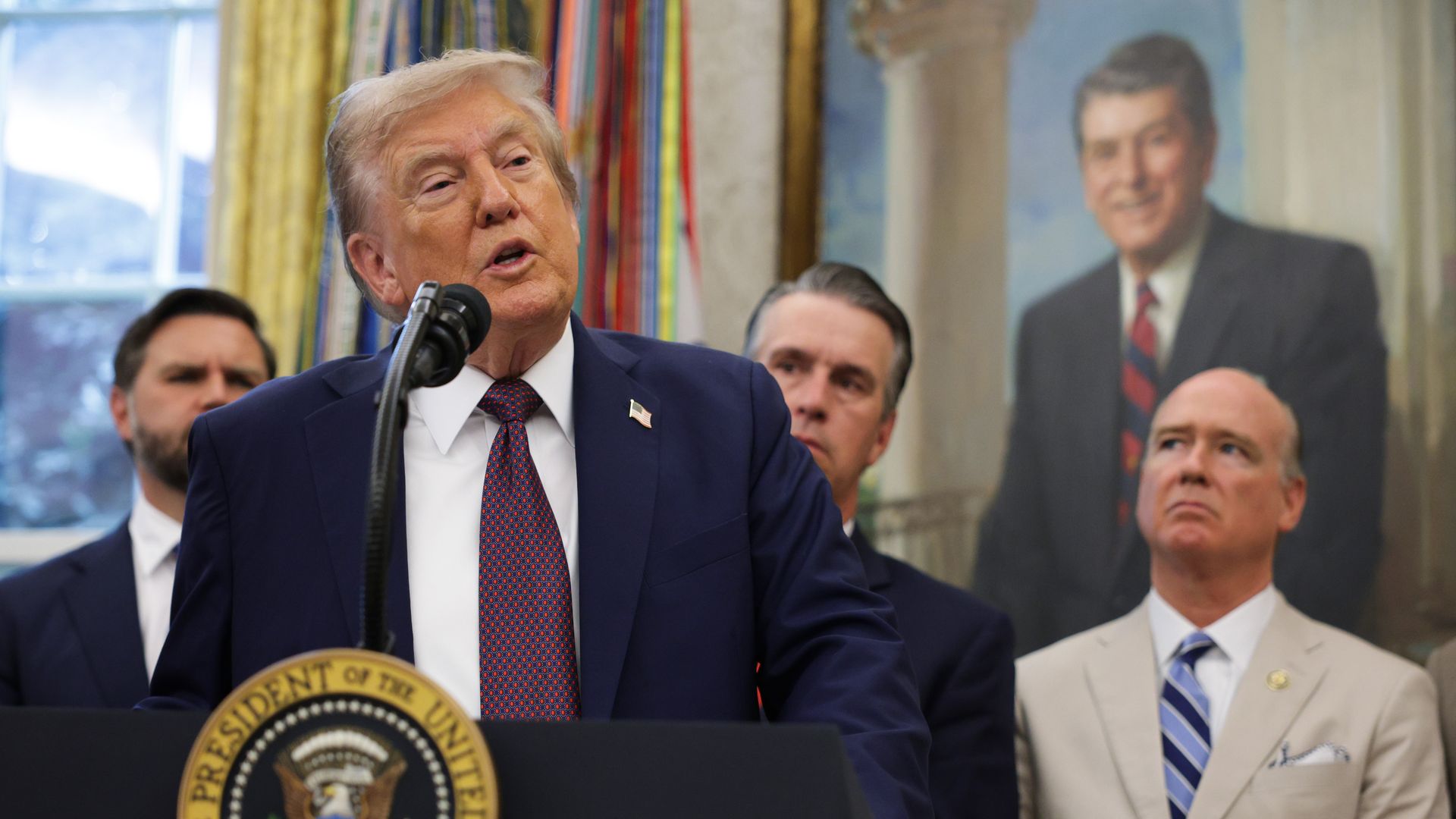Trump speaks into a microphone at a lectern with other lawmakers standing behind him