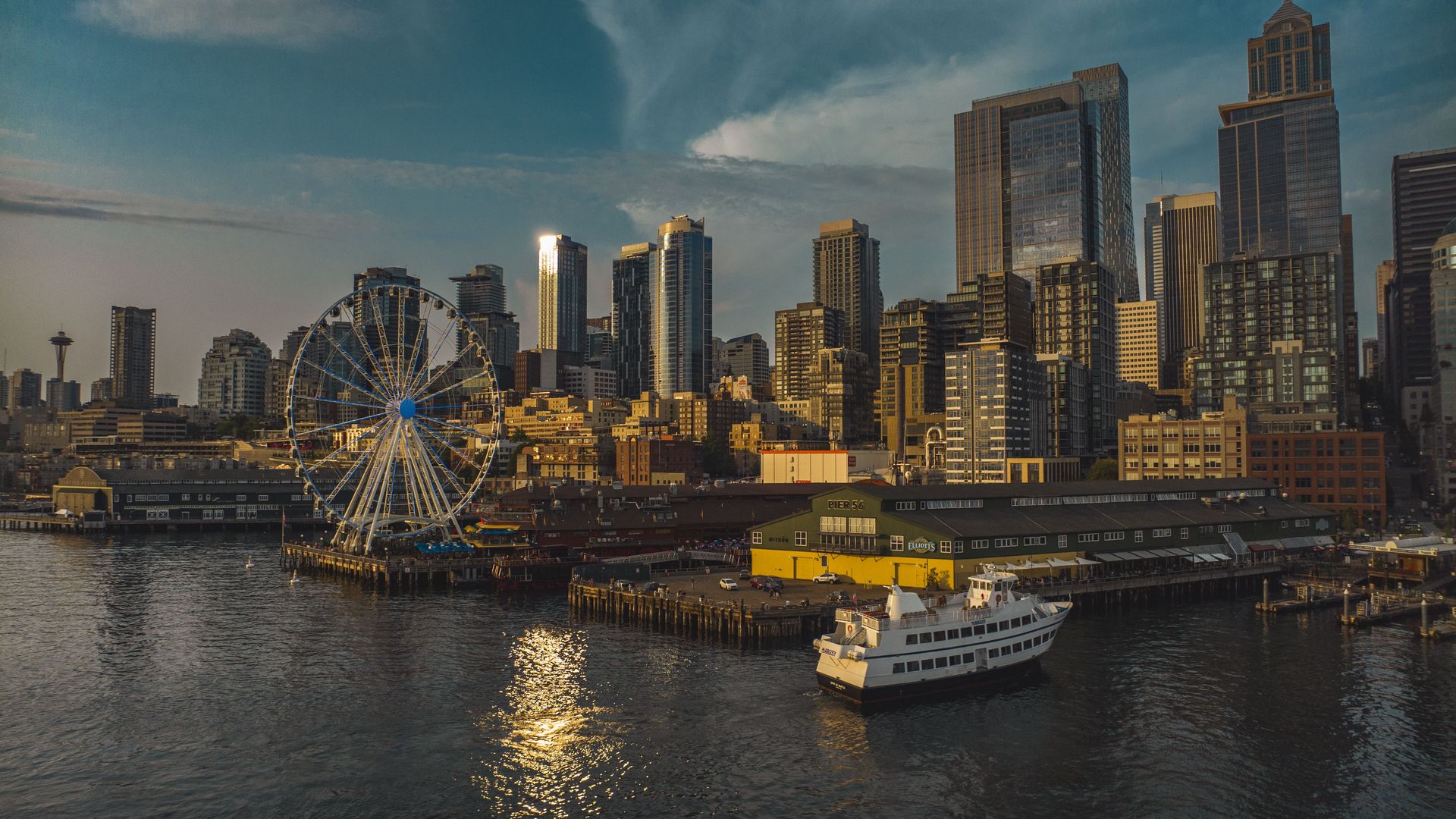 A photo shows the Seattle skyline at sunset with golden light cast on skyscrapers and a ferry pulling into the harbor.