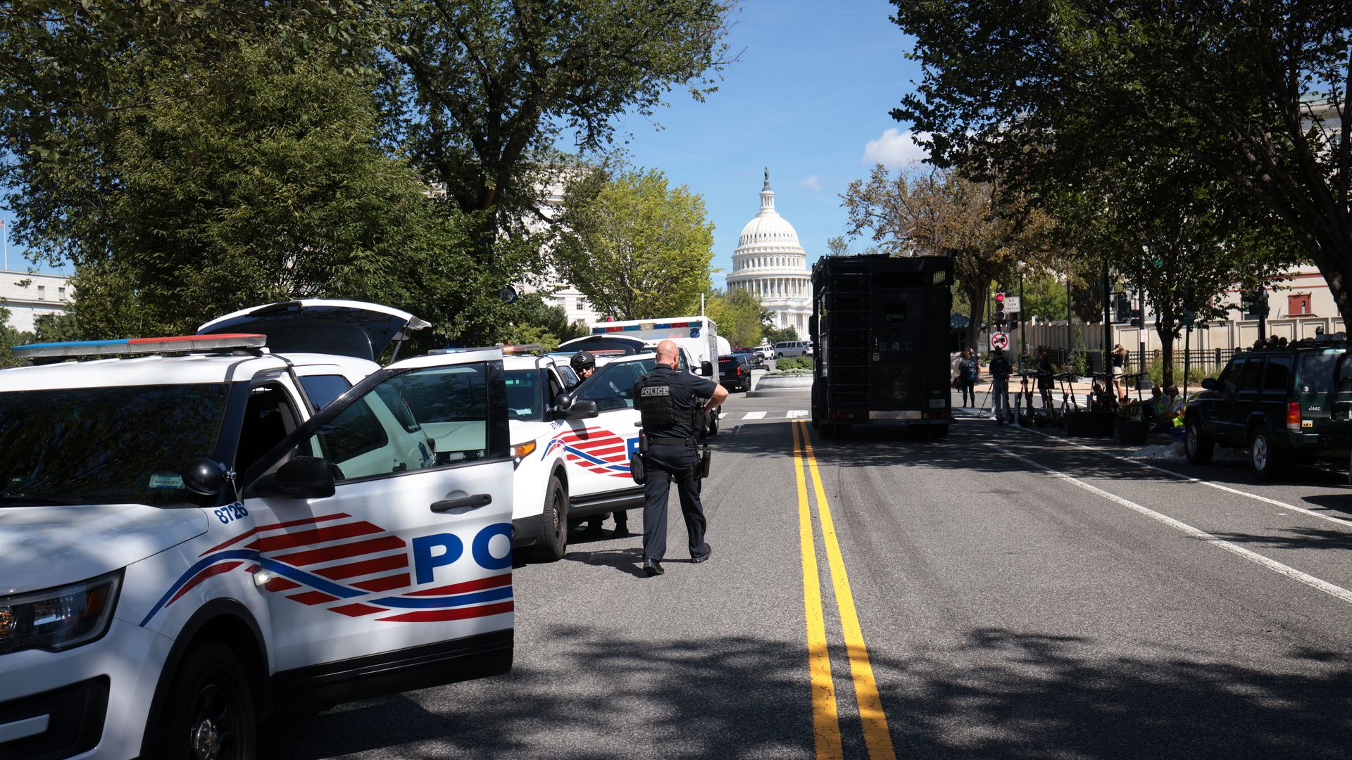 Photo of police cars and first responders lined up along the road with the Capitol building in the distance