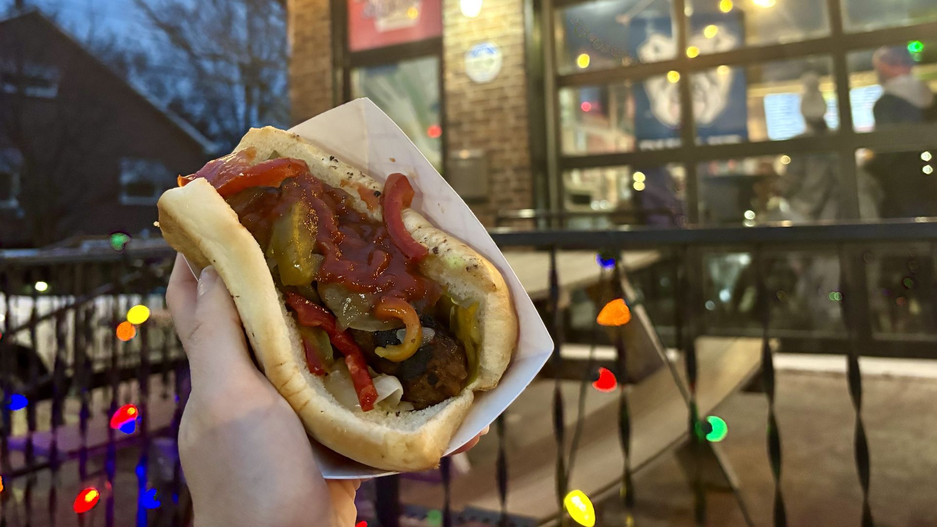 A sausage on a bun held in front of a restaurant