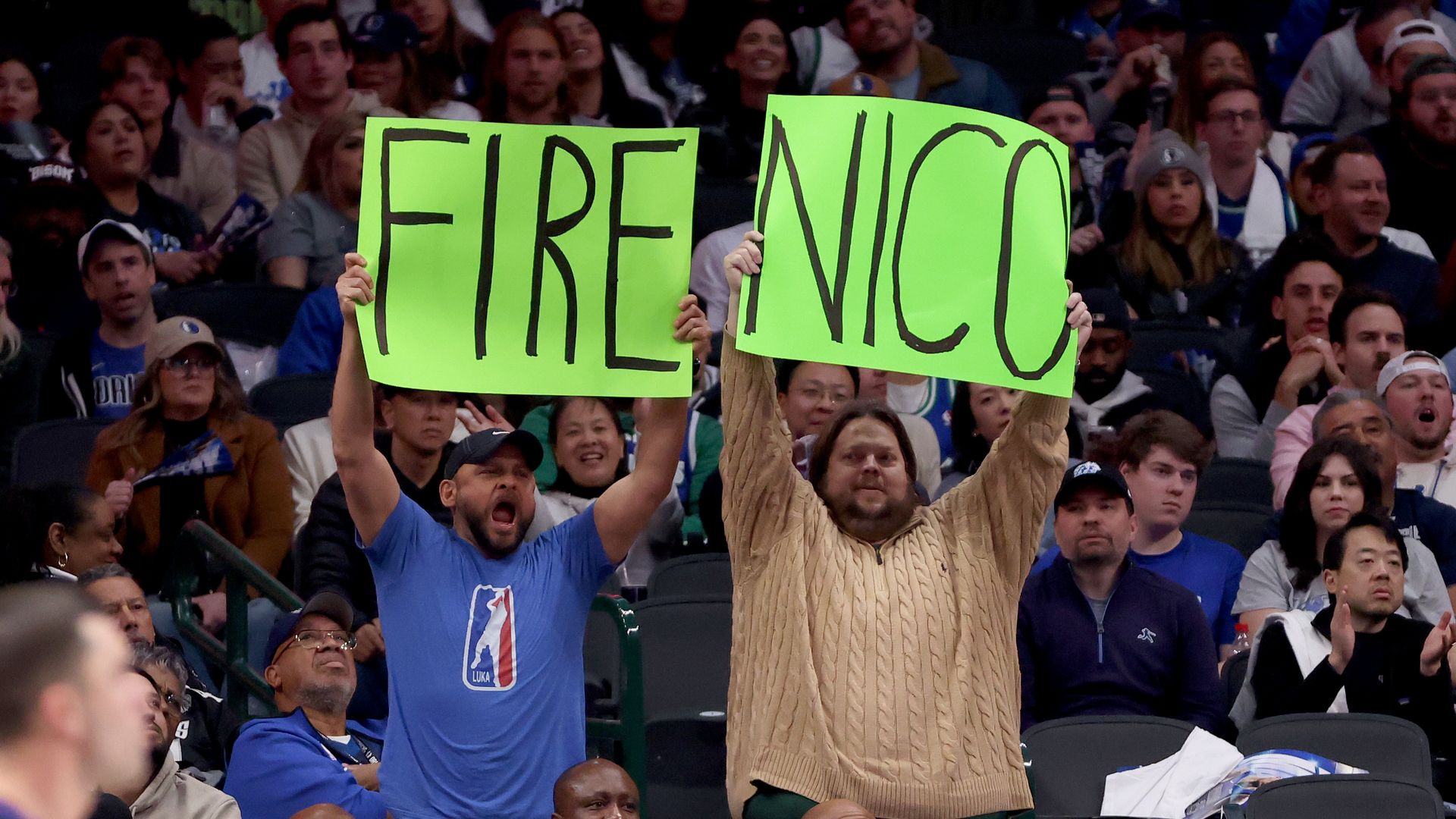 Two men hold "Fire Nico" signs in an arena