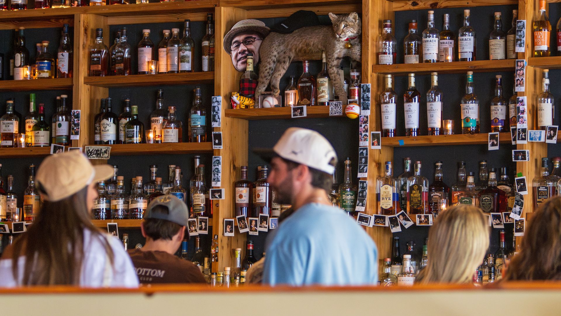 People wait to order drinks at a bar. The back-bar is stuffed with dozens of whiskey bottles.