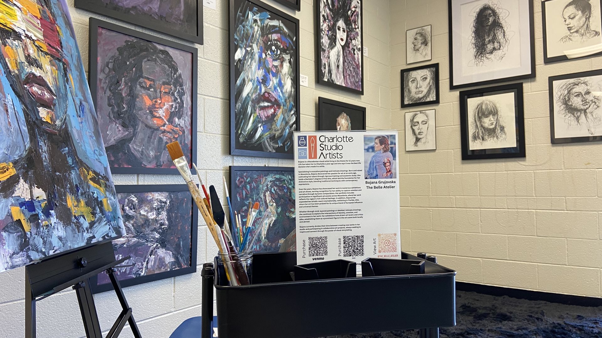 Bojana Grujovska's studio at Charlotte Studio artists. Artwork sits on an easel in front of paint brushes. Paintings and sketches hang on the studio walls.