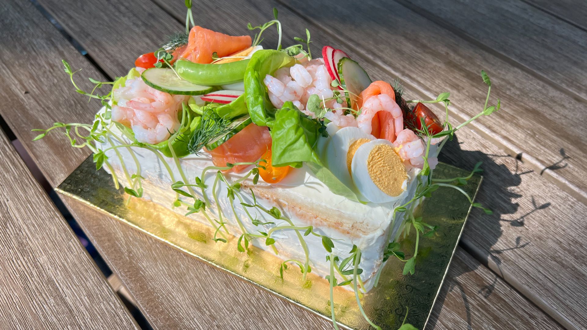 An elaborate cake topped with eggs, shrimp, salmon and greens.