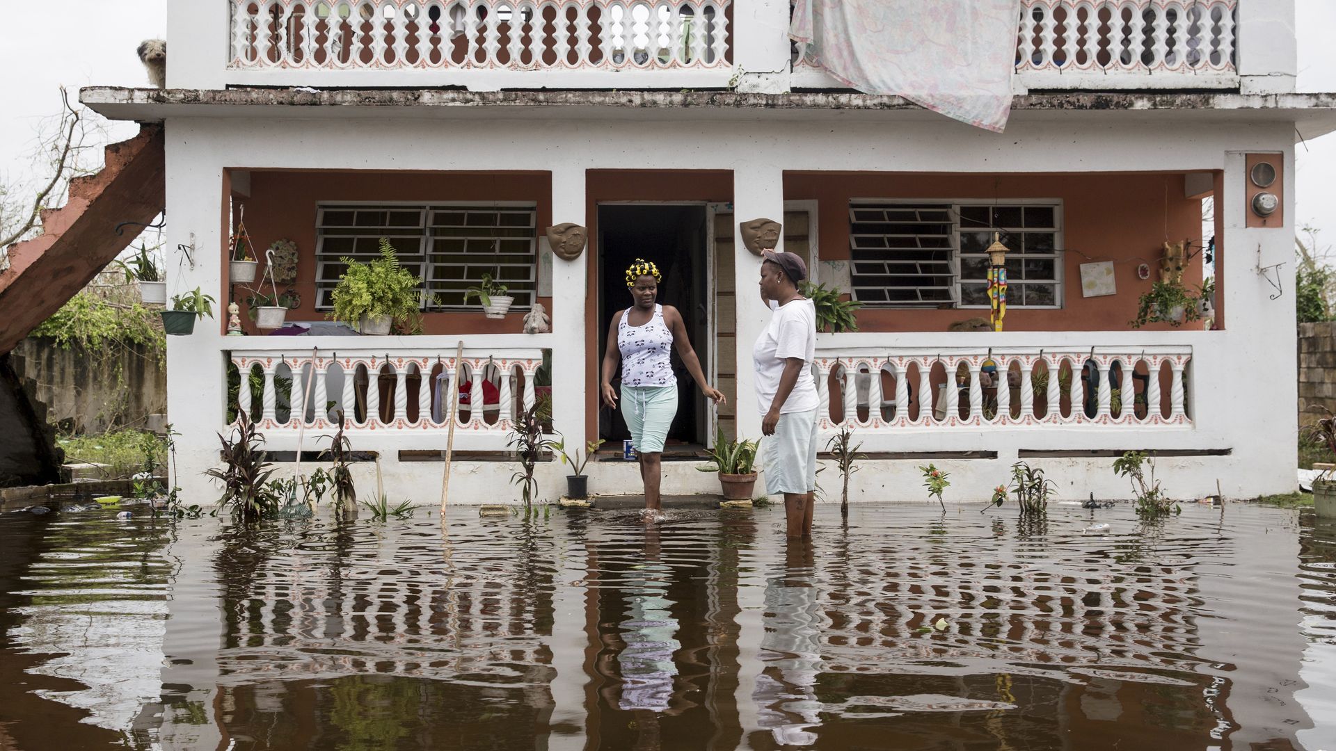 A woman in Loiza, Puerto Rico, walks out of a large white home to a flooded street as a man walks through. 