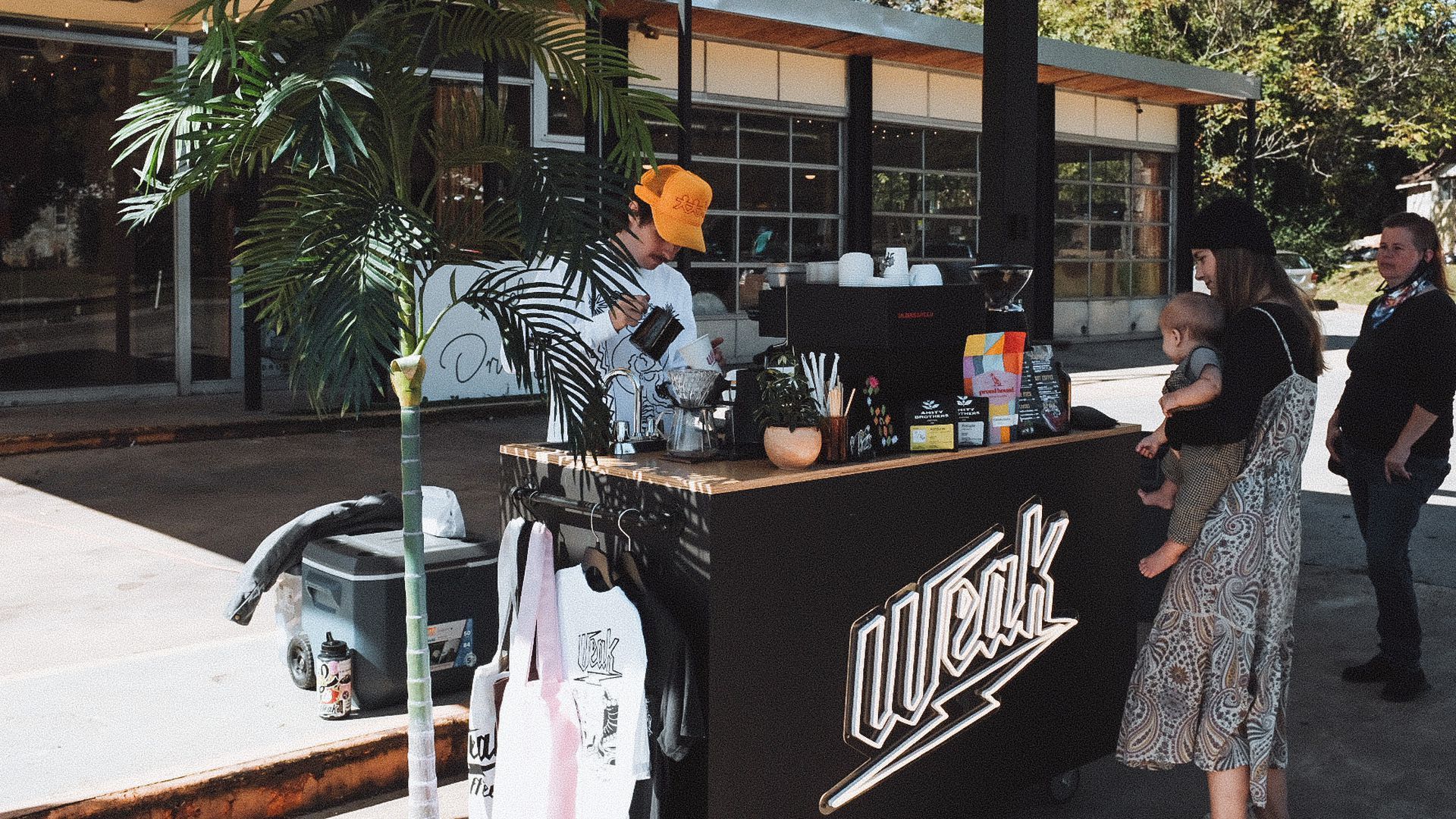 An employee at Weak Coffee pours a coffee for a woman holding a baby.