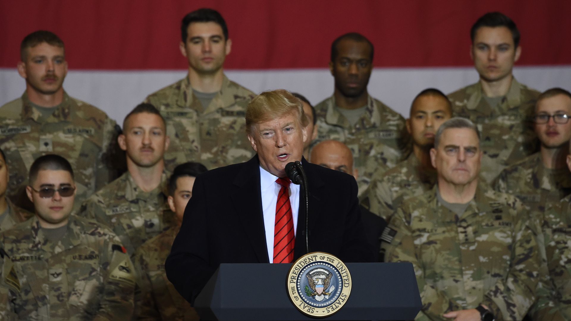 In this image, Trump stands in front of two rows of soldiers at a podium.
