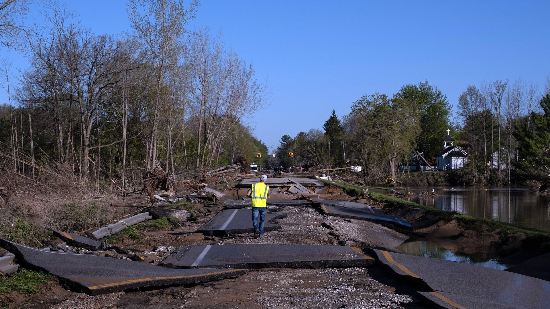 In this image, a man in a yellow caution vest walks down the middle of a highway