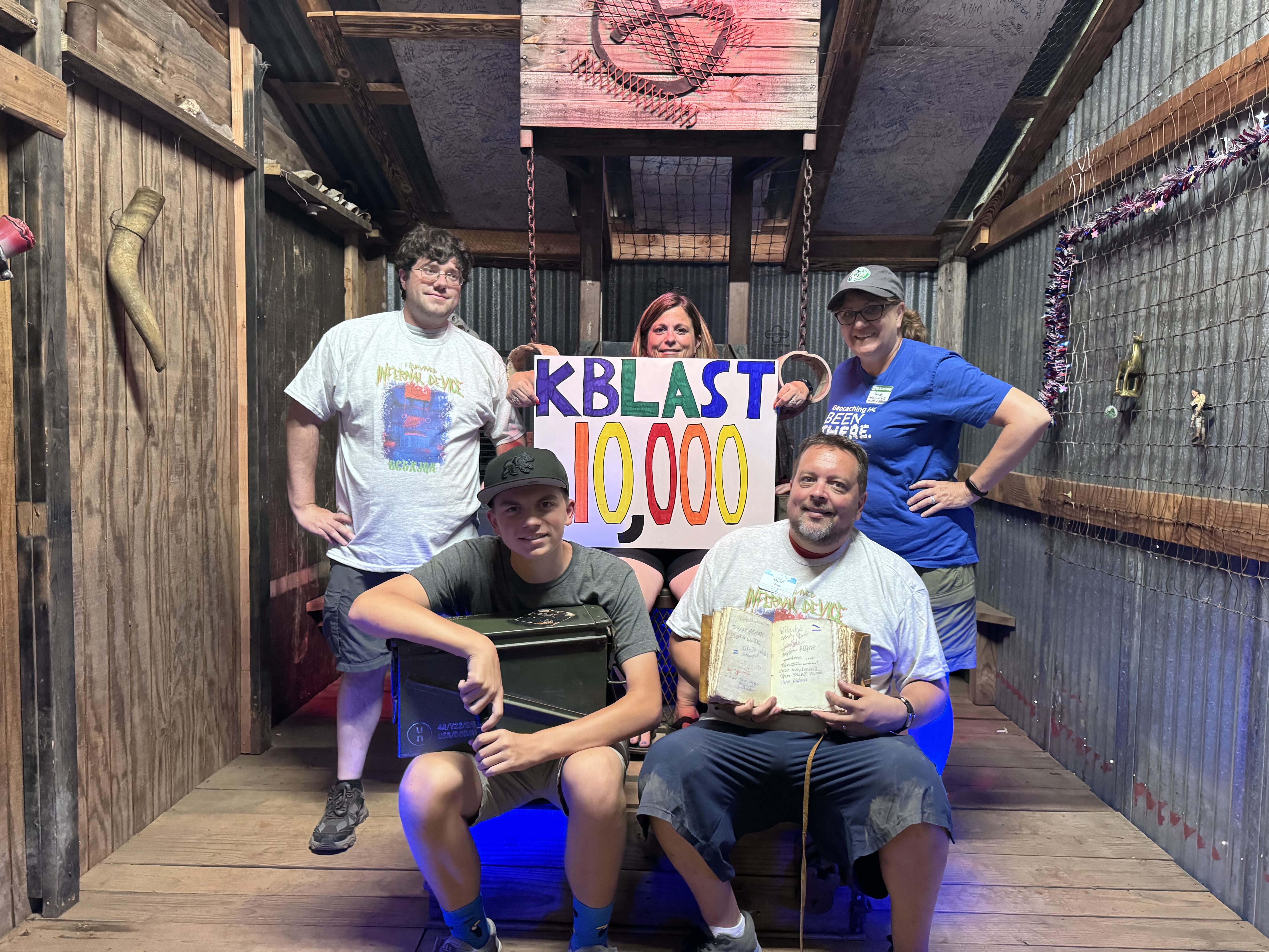 Five people stand inside an escape room holding a sign reading "KBLAST 10,000"