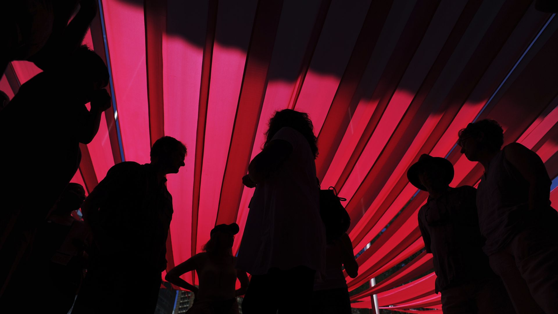 A bright red fabric, where people's silhouettes are seen underneath.  