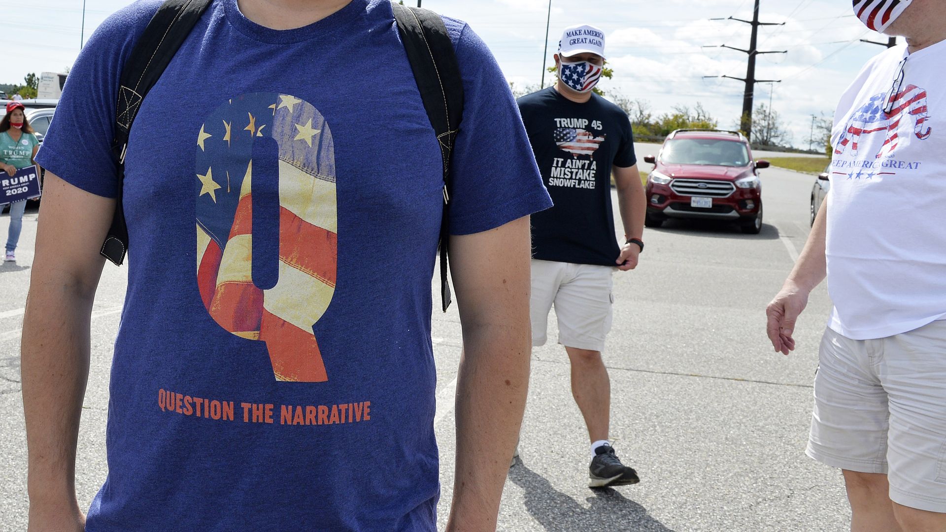 A man wearing a QAnon T-shirt stands in a parking lot