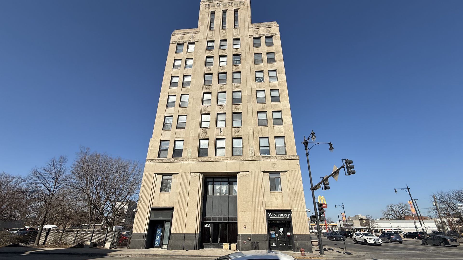 Tall beige Chicago building with Wintrust Bank on the street level, cars on intersection, and clear blue sky during daytime.