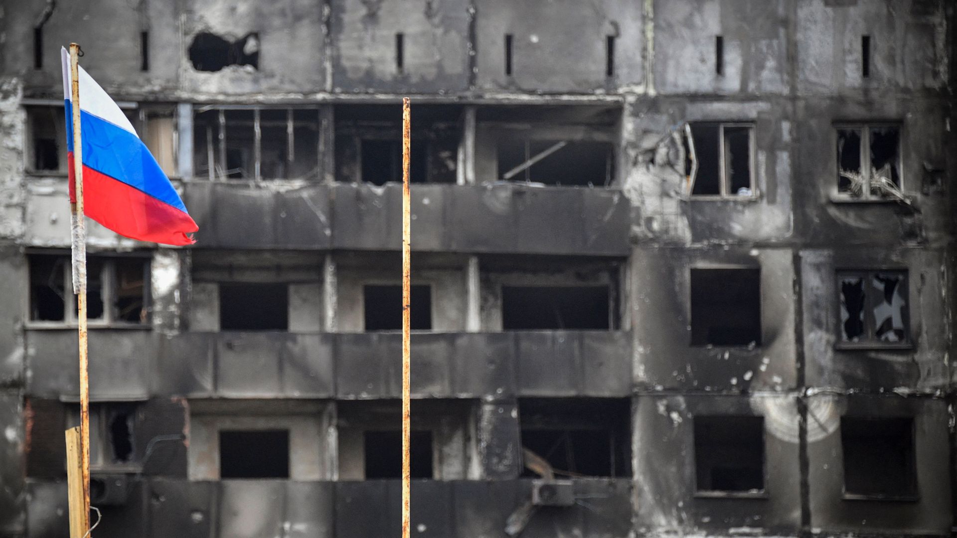 Photo of a Russian flag next to a destroyed building