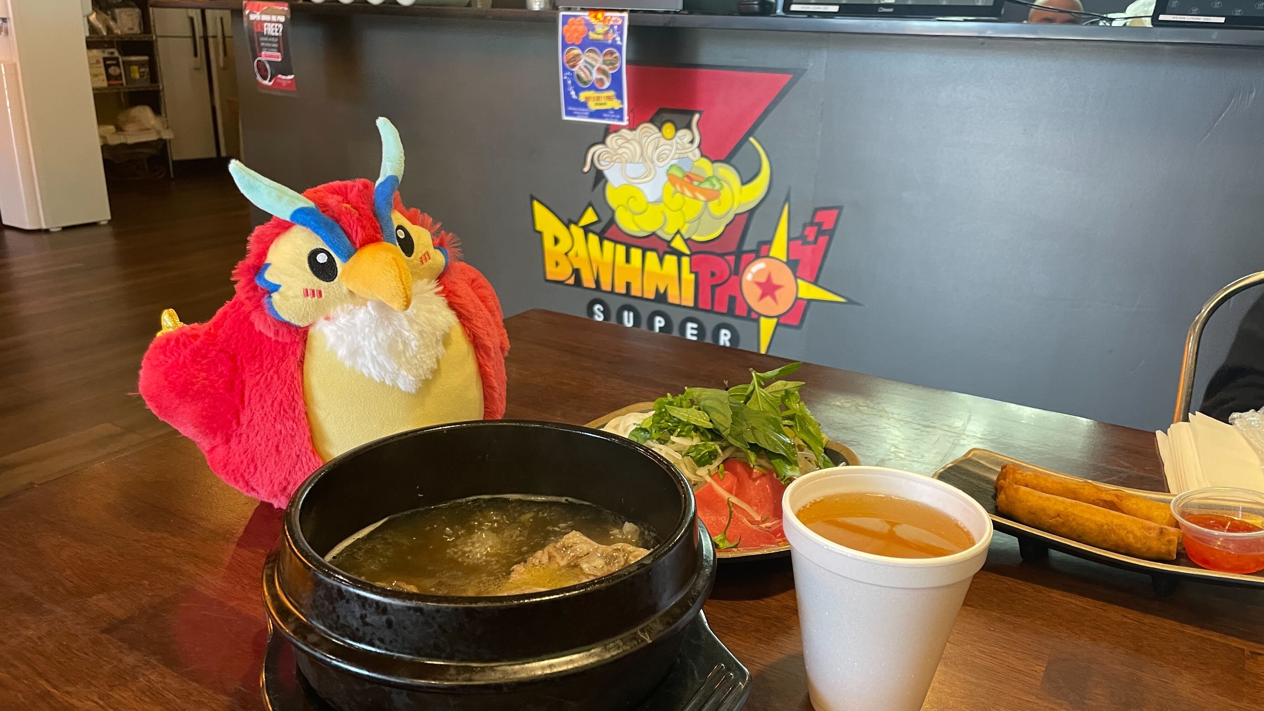Axios Atlanta's mascot, Phoenix 3000, sits on a table in front of a boiling pot of Vietnamese noodle soup. 