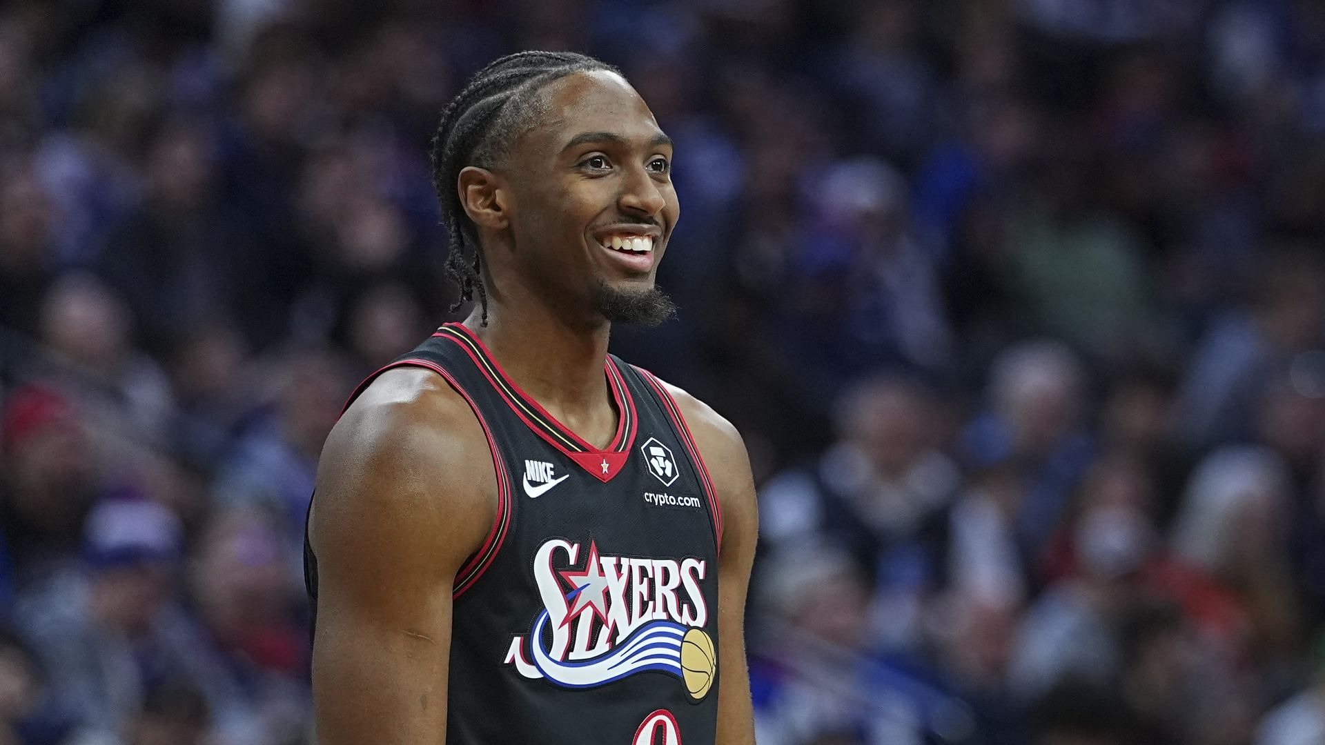 A man wearing a basketball jersey and smiling while standing in front of fans. 