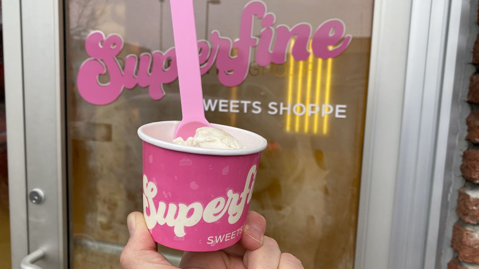 A pink cup holds ice cream with a pink spoon sticking up. 