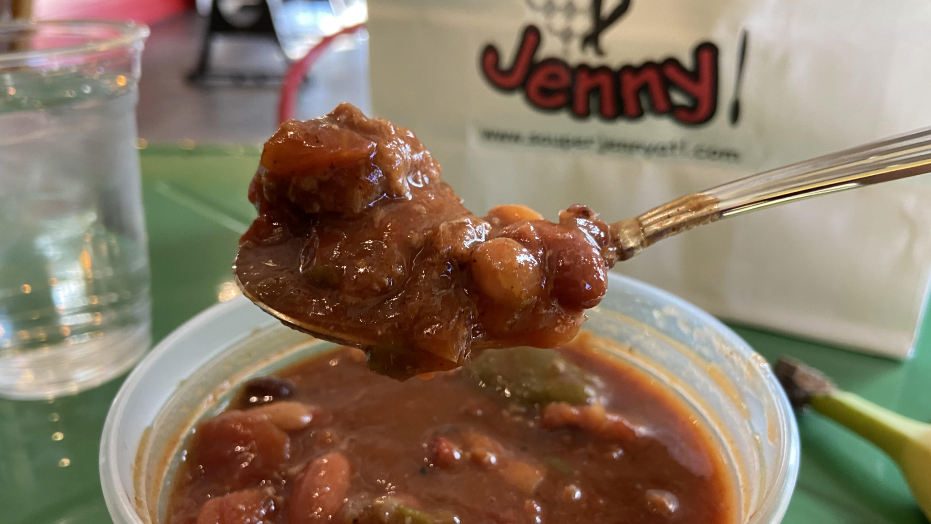 A close-up of turkey chili in a plastic cup on a green table with a bag in the background