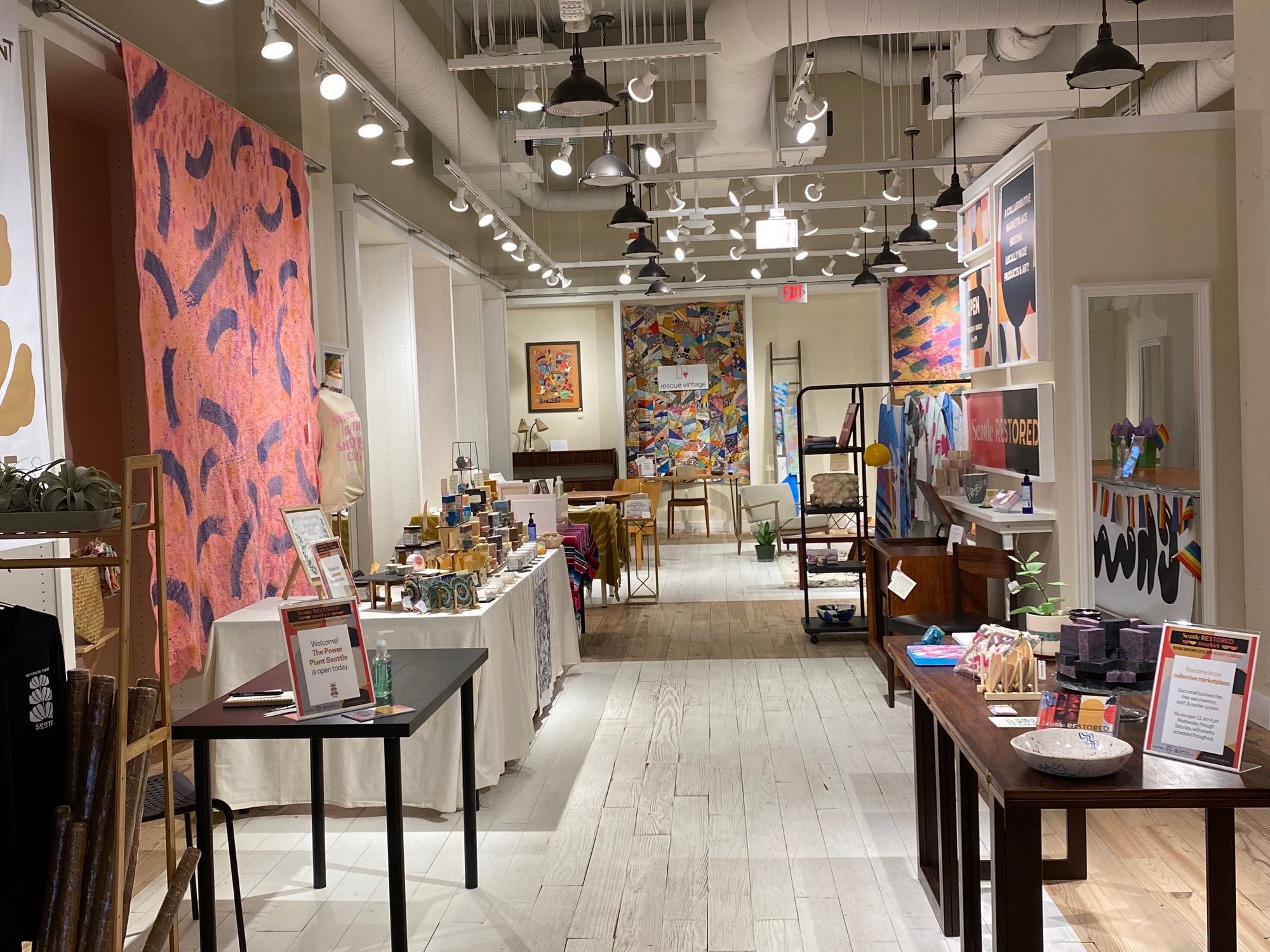 A view of tables laden with goods and art hanging on walls inside a store.