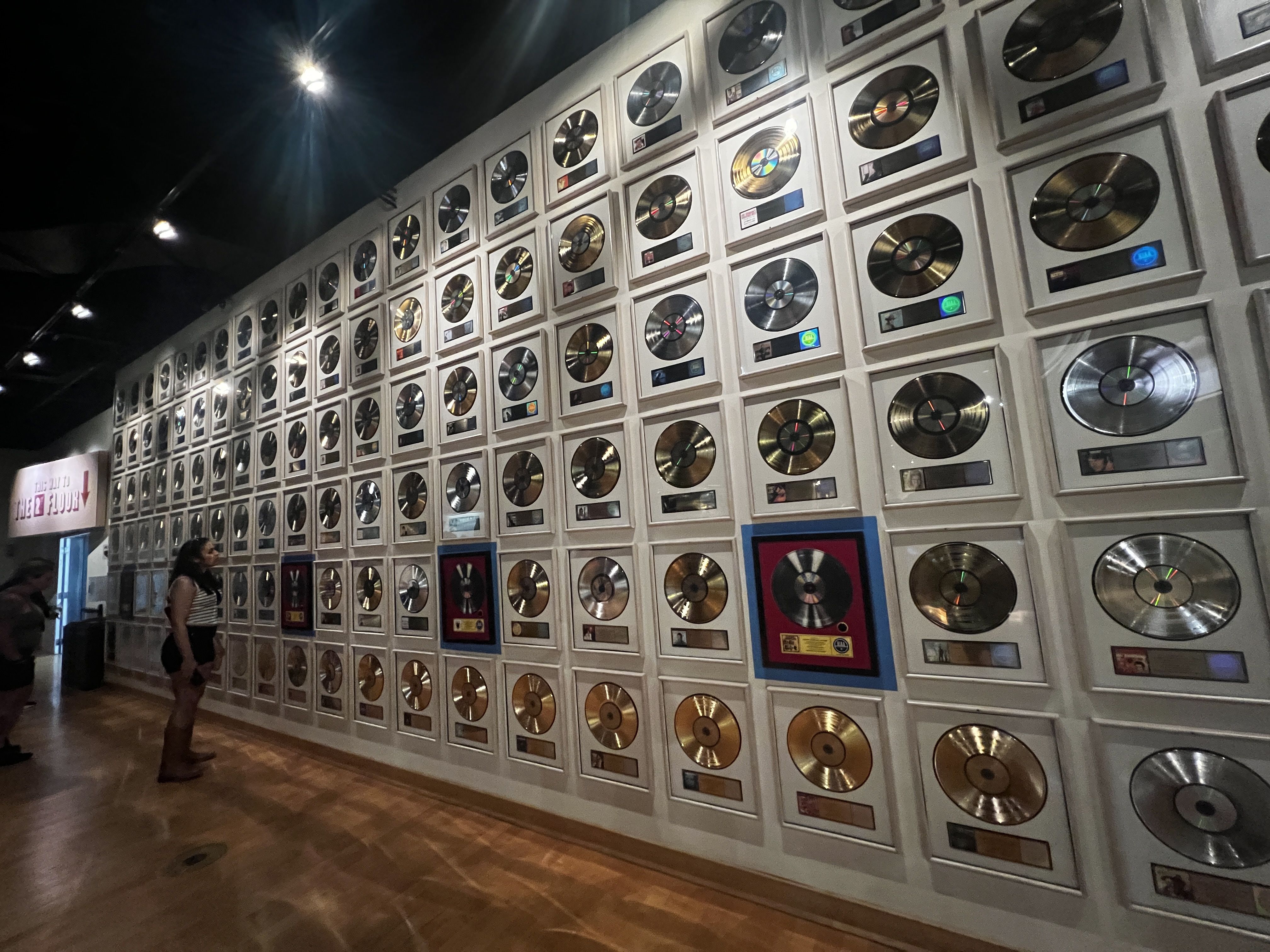 A woman looks at a wall full of gold and platinum records. 