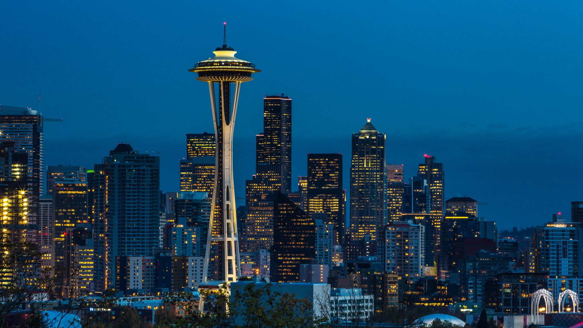 The Seattle skyline with the Space Needle at center, shown with a blue sky turning dark.