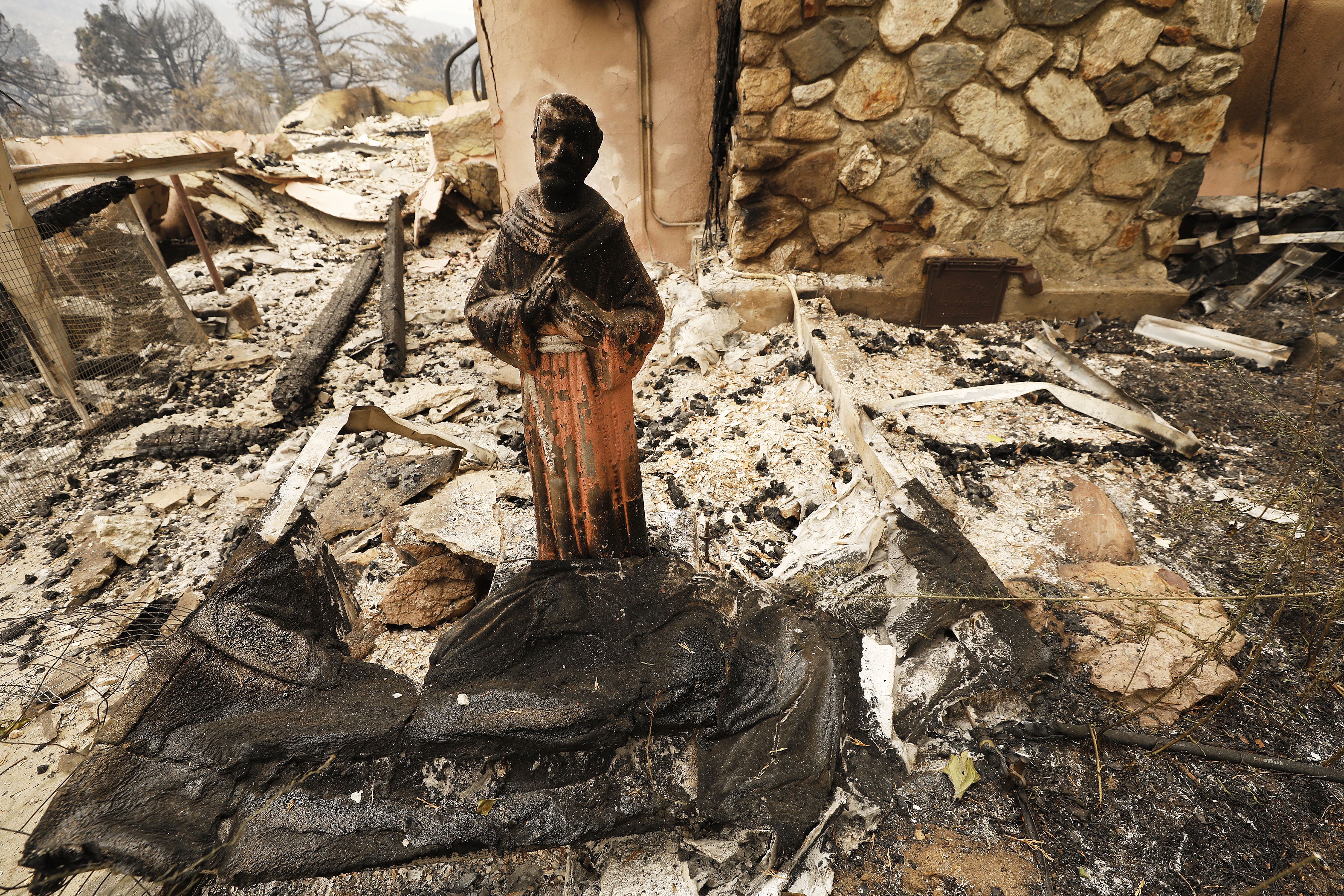 A scorched statue stands in front of a home on Pine Canyon Road destroyed by fire along as several homes, out structures and other vehicles have been destroyed 