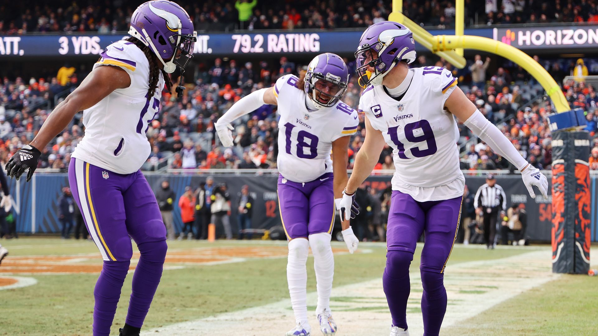 Three Minnesota Vikings players in white and purple uniforms on a football field.
