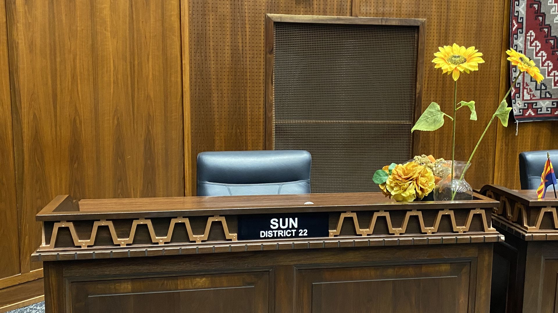 An empty desk with sunflowers on it and a nameplate that reads Sun District 22.