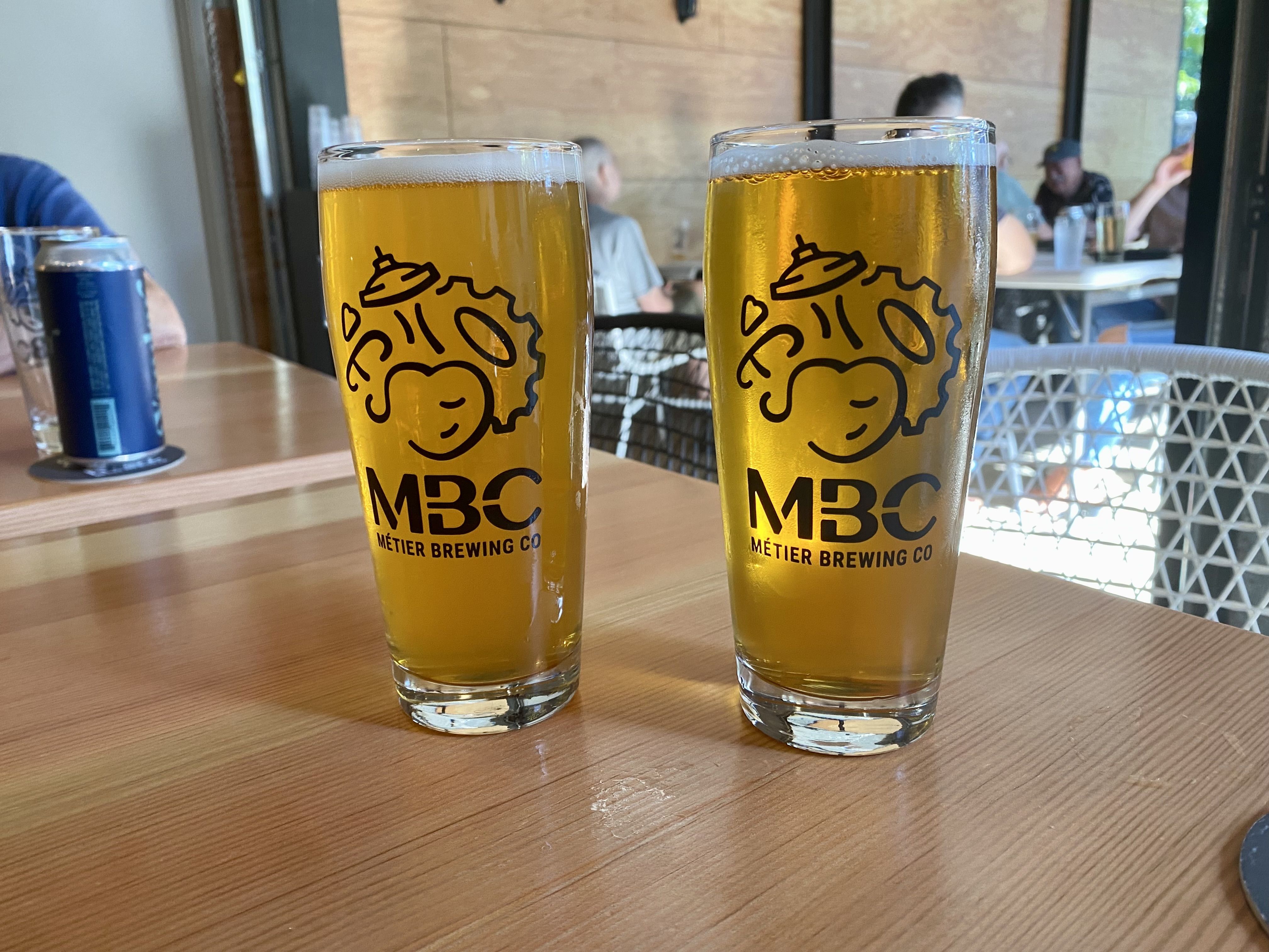 Two tall glasses of beer with label MBC on them.
