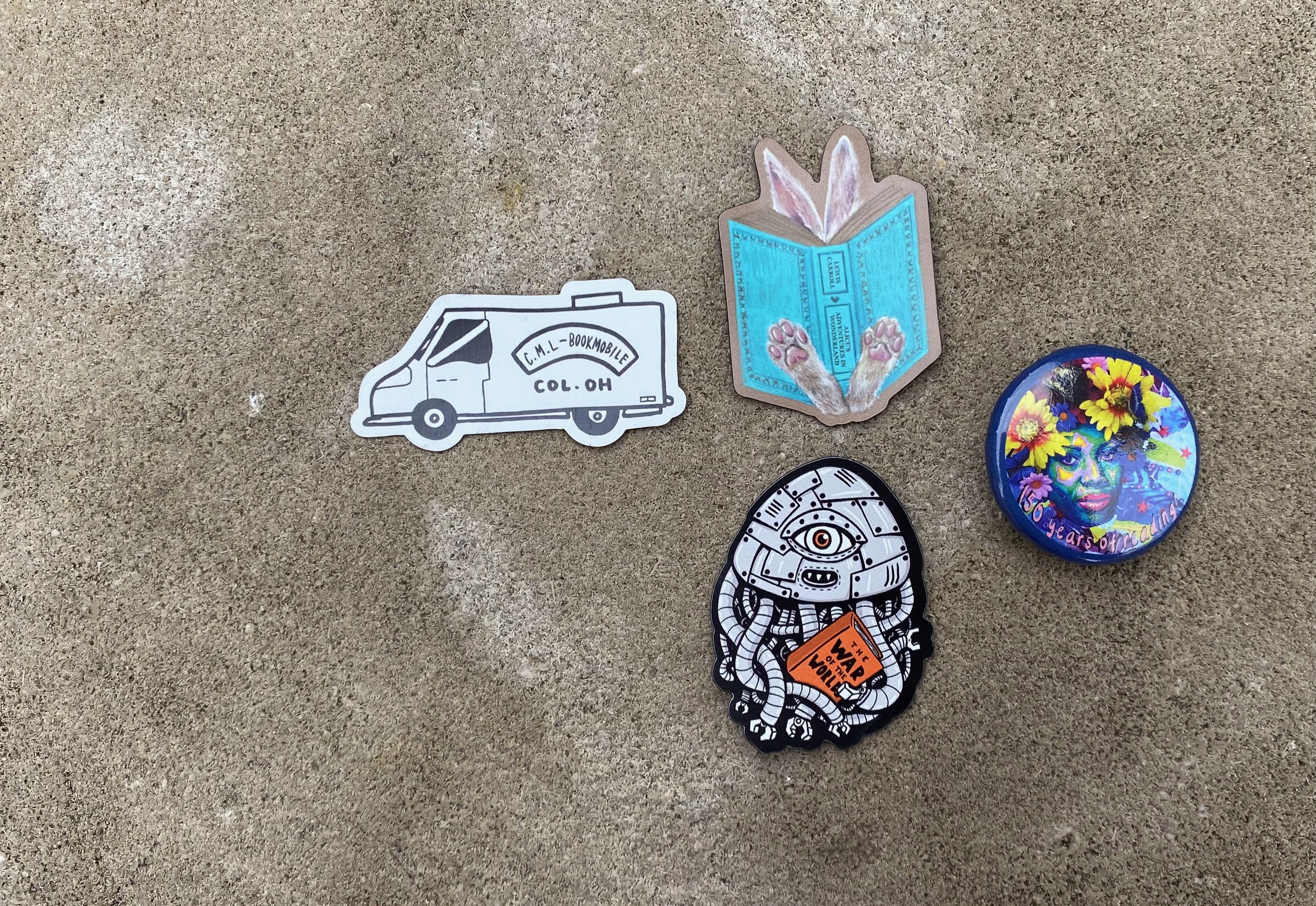 A floral button and four tiny magnets - a Bookmobile, a War of the Worlds alien and a rabbit reading Alice in Wonderland