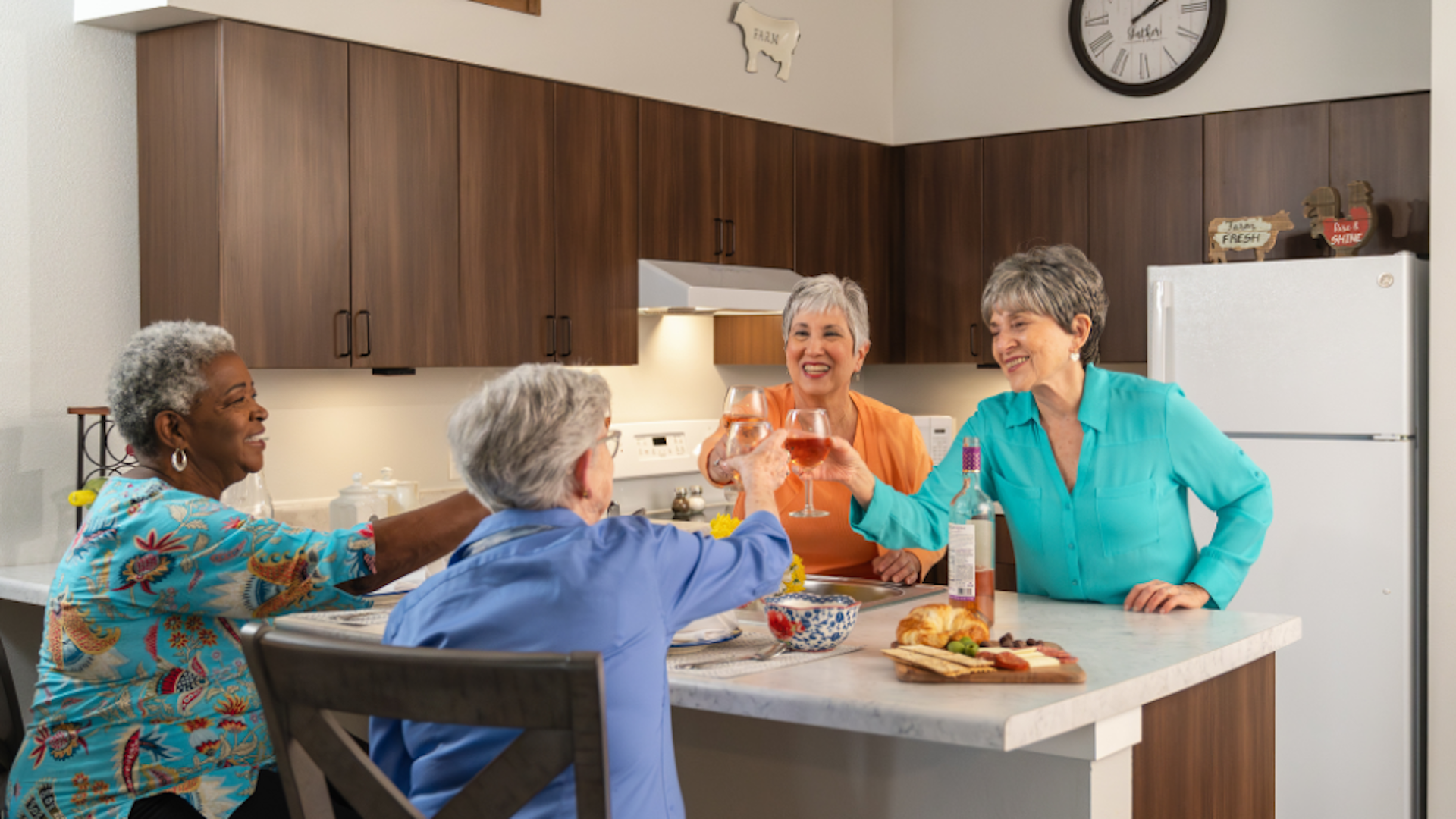 Four women toasting with glasses of wine in a kitchen.