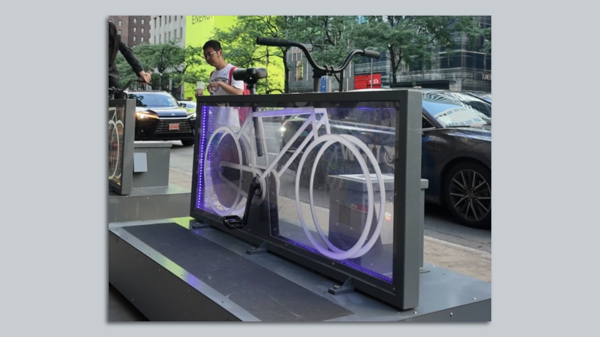 Black border around clear glass with a stationary bike inside it, sitting on a pedastal.