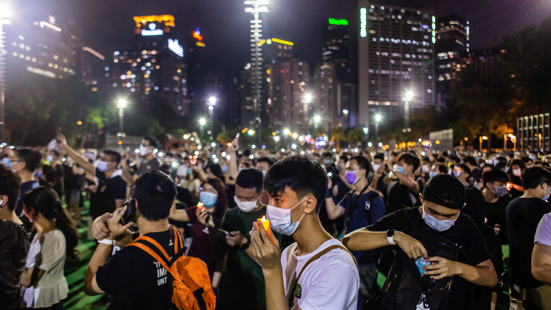A man holds a candle close to his face while wearing a face mask