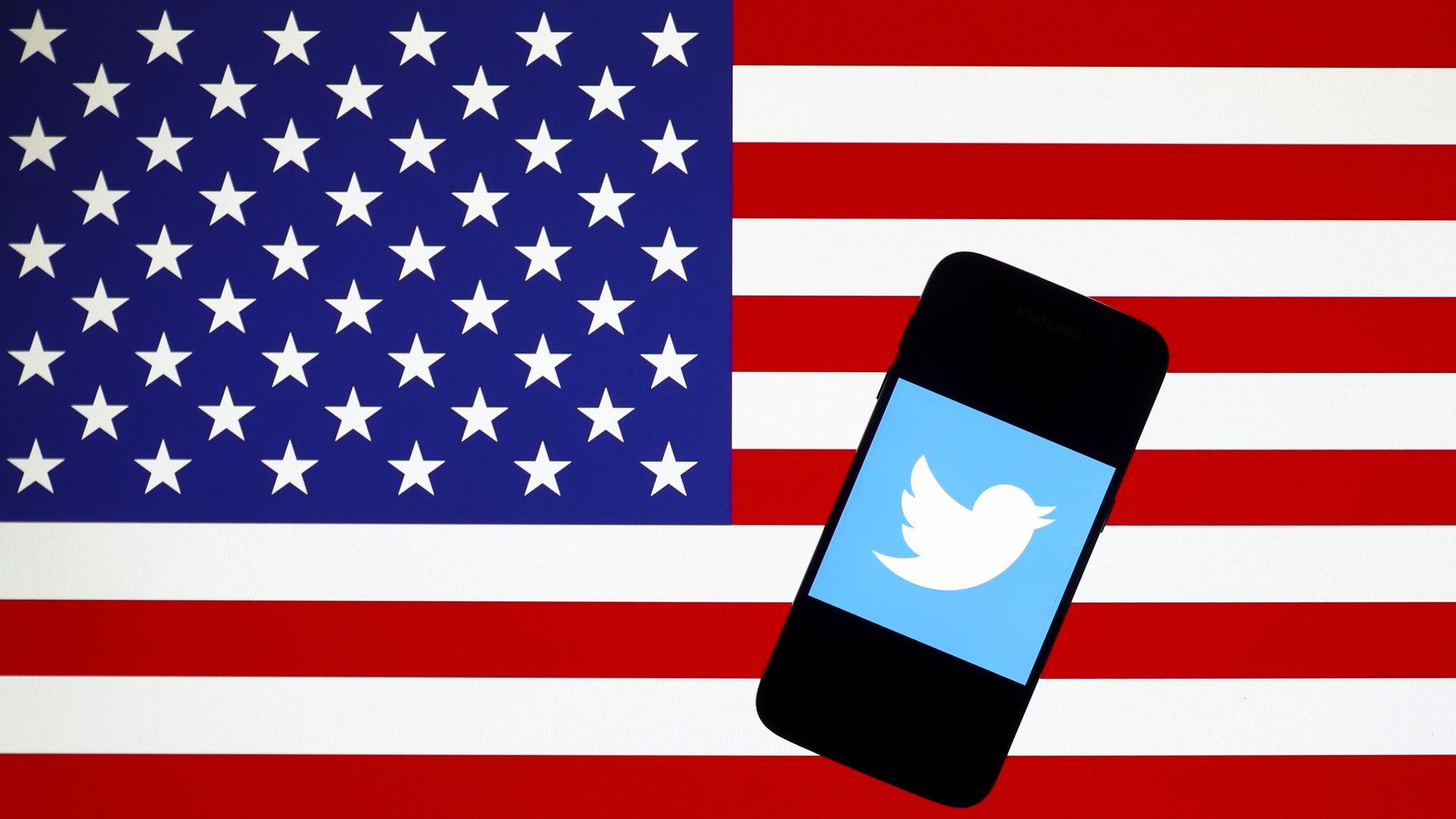 A phone displaying the Twitter logo appears atop the American flag