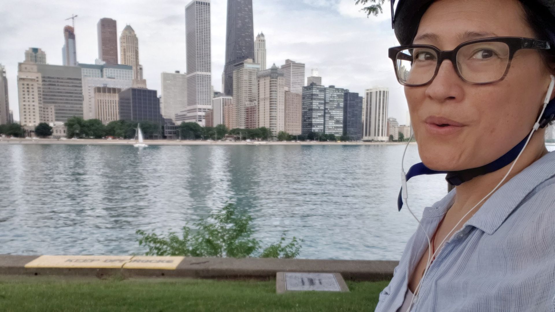 Photo of a woman on her bike in front of a body of water and a city skyline. 