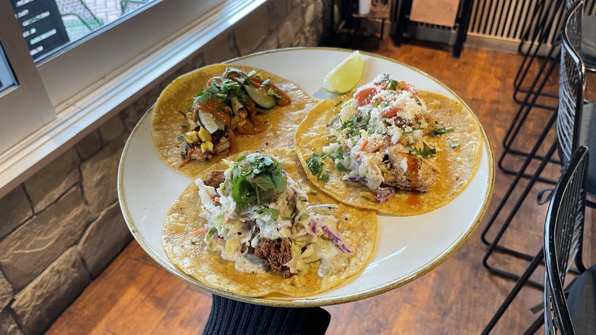 A photo of a person holding a plate with three tacos on it.