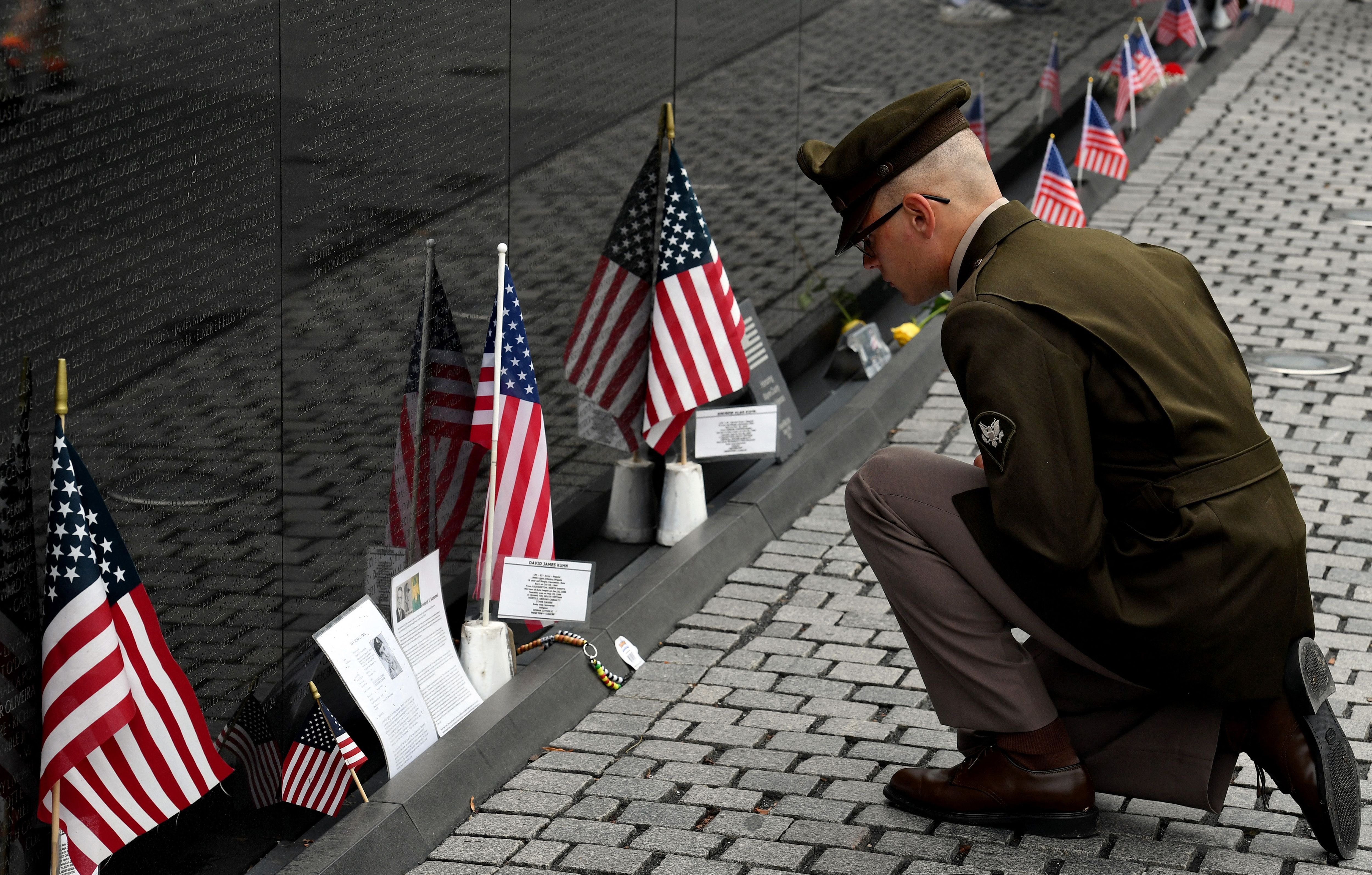 A man in uniform leans down to read names on a plaque surrounded by small American flags